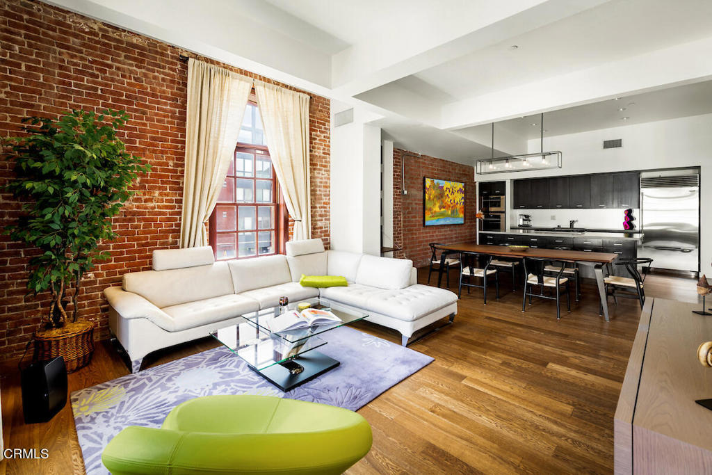 Urban Serenity at the Barn Lofts | Prime Arts District End Unit. Discover a rare blend of industrial character and modern comfort in this stylish end unit at the highly coveted Barn Lofts in the vibrant Arts District. Flooded with natural light, the residence showcases exposed brick walls, warm hardwood floors, and an inviting, open layout. The flexible first floor live/work space offers a variety of uses from a private office or a bedroom, with a separate office, full bath and endless creative potential--ideal for artists, entrepreneurs, or anyone seeking versatility. A mezzanine provides the perfect space for an additional office, reading lounge, or studio. Upstairs, the main living level features a spacious kitchen that flows seamlessly into the dining area and living room, creating an ideal setting for entertaining. A welcoming foyer, powder room, laundry, and walk-in pantry complete the floor.The top level is devoted to the expansive primary suite, which opens to a wrap-around terrace with sweeping city views--a perfect retreat for morning coffee or evening relaxation.Additional highlights include Two assigned indoor garage spaces by entry to the townhome Ample guest parking in a gated area just outside your front door One of the most architecturally distinct buildings in the district Steps from LA's top restaurants, cafes, boutiques, galleries, and the Metro. Located in a close-knit community, this is a rare opportunity to live and work in one of LA's most dynamic neighborhoods.
