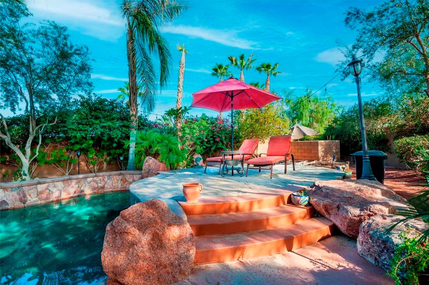 Once upon a time is the way this storied Trilogy at La Quinta property begins. An adult playground of grand scale hidden behind a tall wooden door is a home purposefully designed for the joy of living large. At 2,789 SQ FT, this rare four-bedroom, four-baths Mesquite model home with two-car and separate single car garages, has at its center a large private courtyard with separate doors to the main home, a detached Casita with kitchenette and full bath, and a separate attached Casita, also with a full bath. The exquisite primary bedroom retreat has direct access to the courtyard, and to a private covered back patio. The double-door entry, tray ceiling and room size is outstanding, but the highpoint is a sumptuous bath featuring two separate vanity stations covered in marble and each with walk-in closets, a king-size marble shower with two shower heads and bench seat, and a dreamy soaking tub. Inside, the home is open with ten-foot ceilings, crown molding and tile floors in the main living areas. The great room has custom built-ins, and TV with surround sound in the ceiling and a gas-log fireplace to curl up by while reading or binge watching your favorite shows. The kitchen is outfitted with premium stainless steel appliances, six-burner cooktop, double-oven, and dishwasher. A center island with pendant lighting, abundant cabinetry, built-in pantry and smooth granite slab countertops with stone backsplash makes cooking pure joy. Special occasions call for a formal dining room, and this one is spacious and inviting. The large office area with wine-storage is also usable as a flex space for crafts, wine-room, cafe or anything else your heart desires. The expansive courtyard has seating for large gatherings, and the beautifully crafted pergola adds a filtered cover for year-round comfort. Come fall and winter everyone will enjoy gathering around the raised gas lava-stone firepit while cheering on their favorite teams on the outdoor big screen TV. On warm days, life outside stays comfortable with a Kool Fog misting system that envelops much of the home's exterior in a fine cooling mist. Adjacent to the courtyard, surrounded by exquisite pygmy palms and tropical flora, is a spectacular resort-style Pebble-Tec salt water pool with towering rock waterfalls cascading over three-tiers into the spa and pool below. At the far end of the pool is a raised deck to relax and take in the views, or as a stage to dance the night away.