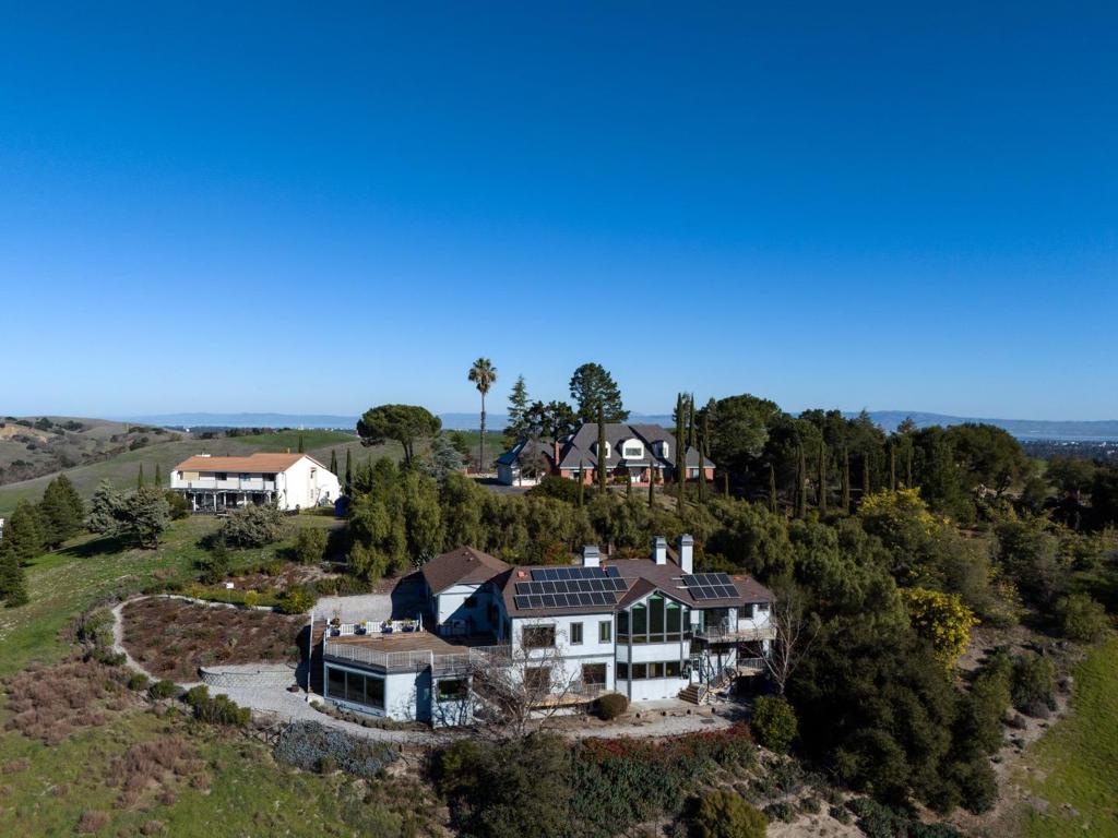Spanning approximately 2.4 acres with breathtaking views, this storybook home is classic and timeless introduced by a signature stone turret with leaded glass details. Fine hardwood floors and matching millwork and cabinetry are complemented by hewn beam ceilings, granite finishes, and expansive windows that invite the views in. Highlights of the solar-powered 5-bedroom, 5.5-bath home begin with a dramatic living room, separate sitting room, formal dining room that opens to a tremendous view deck, plus a kitchen and family room combination. A large guest suite rounds out the main level while the lower levels unfold with four additional bedrooms including a vast primary suite with glorious views. The lower level also has an amazing multi-person customized office ideal for remote work needs. Other features include a wine room and a sauna room. With top-rated Palo Alto schools and a prime location just minutes from Highway 280, this home offers timeless elegance in the heart of Silicon Valley.