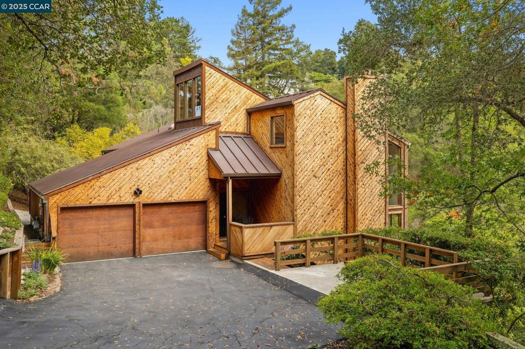 This custom residence, designed by Lemkuhl Construction with interior design guidance from John Wheatman & Associates, showcases striking diagonal wood siding, expansive windows w views, skylights, and decks that blur the line between indoors and out. With 4 bedrooms and 3 baths, including two ensuite retreats, the home balances sophistication with comfort. The vaulted living room features warm diagonal wood detail, a cement fireplace with wood mantel and raised hearth, and dramatic picture windows framing Orinda hill views. A loft with floating cedar shelving adds a refined modern vibe. The dining room includes custom built-ins with slatted doors concealing cabinetry, shelving, and a bar sink. The adjacent light-filled kitchen offers walnut cabinetry, Corian counters, Sub-Zero refrigerator, double ovens, pantry, and open pass-through to dining—perfect for entertaining. The lower-level ensuite opens to a private deck, while the spacious primary retreat enjoys a walk-in closet, spacious bath, and private deck with hillside views. Minutes to Orinda Country Club, Lake Cascade, trails, BART, top-rated schools, and just 20 minutes to San Francisco.