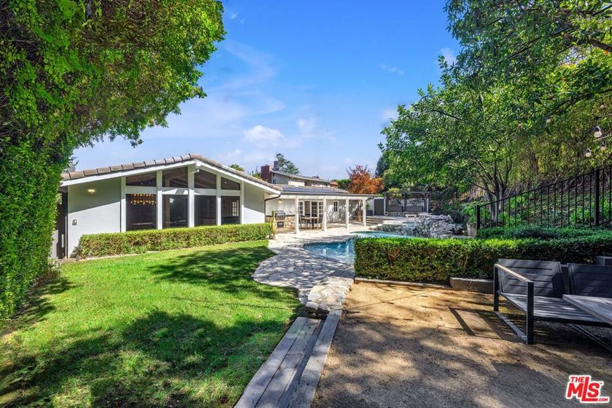This exceptional 3,556 sq.ft. single-story Mid-Century Ranch, updated with Contemporary finishes, sits behind stately private gates, offering a rare opportunity for an unfurnished minimum one-year lease. Impeccably maintained and blending timeless charm with modern luxury, the home is ideally located in the coveted Laurel Hills neighborhood, within the acclaimed Wonderland Avenue Elementary School district and near the Mulholland Tennis Club. The property offers complete privacy, lush landscaped grounds, and effortless indoor/outdoor living. Inside, you'll find 5 bedrooms and 3.5 bathrooms, including a grand primary suite retreat with vaulted high ceilings, a cozy sitting area with fireplace, a private office nook, a spa-quality bathroom with soaking tub and separate shower, and an expansive walk-in closet. Four bedrooms are thoughtfully positioned on one side of the home, while a private fifth bedroom with its own bath is located on the opposite side  ideal for guests or staff. The expansive step-down living room with pitched beam ceilings, a gas fireplace, and oversized windows flows seamlessly into the formal dining room, a stylish wet bar, and a comfortable lounge. The gourmet kitchen is outfitted with top-of-the-line appliances, granite countertops, a breakfast area, and an eat-in island all opening directly to the backyard for easy entertaining. Newly refinished hardwood floors, fresh paint, wood-paned or triple-paned windows, and elegant lighting fixtures enhance the home's warm yet sophisticated feel. The backyard is a true private oasis, featuring a sparkling heated pool and spa, a sun deck with built-in BBQ, a grassy lawn, and multiple lounging spaces perfect for dining al fresco or hosting. With its flat lot and perfect indoor/outdoor flow, the home is equally suited for relaxed living or large-scale entertaining. This gated retreat not only offers resort-style living but also eco-conscious luxury with solar panels and an EV charging station, helping to keep energy costs low. Located just off Mulholland Drive and minutes from both the Westside and the Valley, this rare offering combines comfort, style, and convenience in one of Los Angeles's most desirable neighborhoods.