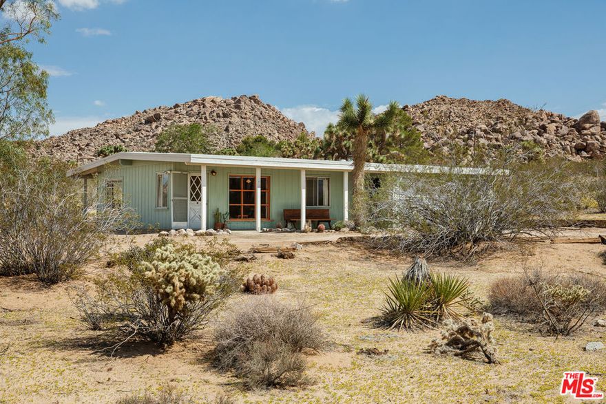 Time to slow down and unwind at Wagon Wheel Hideaway - a 1955 midcentury cabin set on five acres of pristine desert, just five minutes from the entrance of Joshua Tree National Park. Backed against the boulders of Monument Manor, this nostalgic retreat offers a rare opportunity to own a piece of desert history with more than enough space to write a new chapter. Architectural plans have been drawn by the renowned firm Oller & Pejic for a structure that engages in an evocative conversation with the landscape. Cherished by the same family for over half a century, this much-loved vacation home has been a gathering place for holidays and quality time within its cozy two-bedroom, one-bathroom footprint. Attached to the house, a spacious two-car garage includes a storage and bonus room, ideal for a studio or creative workshop. Outside, mature Joshua trees anchor sweeping desert vistas visible from every room. Add a pool, park your Airstream, open up a bygone-era Airbnb, or simply sit back and watch the sky turn orange and violet each evening from the porch- the possibilities are endless. This is the one - a prestigious Monument Manor location, BLM hiking trails up the road, stargazing, close proximity to the buzz of downtown Joshua Tree, and the tranquility of nature right at your doorstep.