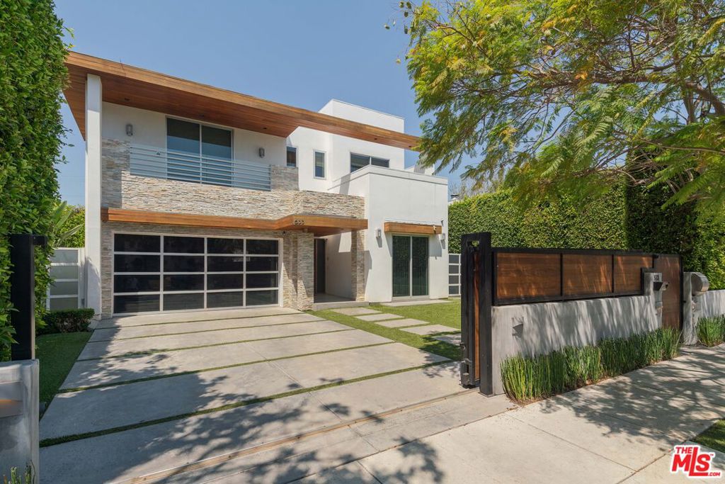 Experience elevated California living amongst one of the largest homes in Beverly Grove. This gated architectural modern is tucked in the heart of Melrose, one of Los Angeles' most vibrant and walkable neighborhoods. Originally built in 2010 and recently enhanced with thoughtful upgrades, this 5-bedroom, 5-bath residence offers sophisticated design, open-concept living, and effortless indoor-outdoor connection. From the moment you pass through the private entry, clean lines, soaring ceilings, and a warm, contemporary aesthetic set the tone. The main level features a light-filled great room designed for both entertaining and relaxed everyday living. Expansive Fleetwood doors vanish into the walls, opening to a lush backyard retreat with a resort-style pool, covered lounge, and built-in BBQ perfect for alfresco gatherings. At the center of the home, a chef's kitchen boasts premium Miele appliances, expansive stone surfaces, custom cabinetry, and a generous island. A sleek built-in bar nearby adds a refined touch for hosting. A private guest suite with its own bath sits on the lower level, ideal for visitors or use as a home office. Upstairs, the primary suite serves as a serene escape with a spa-inspired bath, soaking tub, dual vanities, dressing table, and walk-in closet. Two additional en-suite bedrooms plus a versatile den complete the upper floor. Additional highlights include wide-plank wood and stone flooring, high ceilings throughout, an attached two-car garage, and custom details that balance style with comfort.Just steps from the energy of Melrose Avenue, you're close to acclaimed dining, boutique shopping, and cultural landmarks yet still enjoy the privacy of a quiet residential street. This is turnkey city living at its finest.