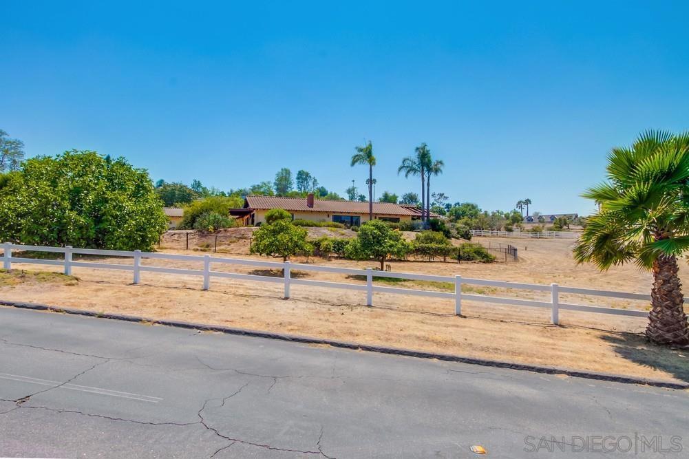 Indulge in panoramic views and breezy coastal weather from this single-level Hialeah Estates home tucked away on a rare, flat 2.6-acre corner lot in the heart of Bonsall’s most established executive neighborhood. This sprawling ranch-style residence offers endless potential with soaring vaulted ceilings, floor-to-ceiling windows, and wood-beamed architecture that brings warmth and character to every oversized room. Beautiful hardwood floors flow throughout, and the spacious great room connects formal and informal living areas—each with its own fireplace. The country-style kitchen opens to a shaded veranda perfect for morning coffee or evening breezes. A charming garden room off the primary suite adds extra space for relaxing or creative pursuits. This is the lowest priced home in Saratoga by over $500,000—offering an exceptional value for anyone seeking land, space, and opportunity. The massive laundry room includes a sink and abundant cabinetry. A 36-panel solar system offsets energy costs, and the attached 5-car garage makes room for your workshop, toys, or car collection. The primary suite is tucked into a quiet corner of the home with vaulted ceilings, garden views, and a breezy, retreat-like feel. The flat, usable lot is horse-legal and primed for your vision—whether that’s a guest house, vineyard, grove, barn, or arena. Grape vines, avocado, fig, grapefruit, apricot, lime, loquat, tangerine and a heritage poinsettia tree create a peaceful agrarian backdrop with plenty of room to expand.