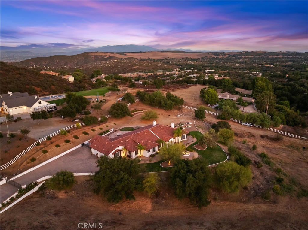 Set on 5.85 acres of mostly flat, usable land, this perfect single story, 3,492 square foot custom estate offers 4 bedrooms and 3.5 bathrooms, located close to the entrance of La Cresta.
The automatic gate opens to over 7,000 square feet of custom reinforced concrete—perfect for RVs, large vehicles, or ample guest parking.
Inside, you’ll find 10-foot ceilings, 8-foot solid mahogany doors, and 18-inch travertine flooring. The gourmet kitchen is designed for both everyday living and entertaining, with cherry cabinetry, a spacious island with prep sink, wine refrigerator, and premium appliances including a Viking cooktop, KitchenAid double convection ovens, built-in refrigerator, and dishwasher. Formal living and dining room areas feature walnut floors and coffered ceilings with ambient lighting. The primary suite offers a spa-like walk-in shower, jetted soaking tub, dual closets, and elegant finishes. Spend time in the 1,130-square-foot 3 car garage that includes a workbench, attic access, unique ceiling fan, and a 30-foot depth to easily accommodate large trucks.
Outdoors, enjoy a built-in Kitchenaid BBQ, fire pit with ambient lighting, terraced landscaping, and a covered patio perfect for year-round gatherings. A 22kW Generac generator provides automatic backup power for peace of mind.
21977 Paseo Chico delivers the best of country living in the prestigious community, La Cresta, with quick access to wineries, restaurants, and shops.