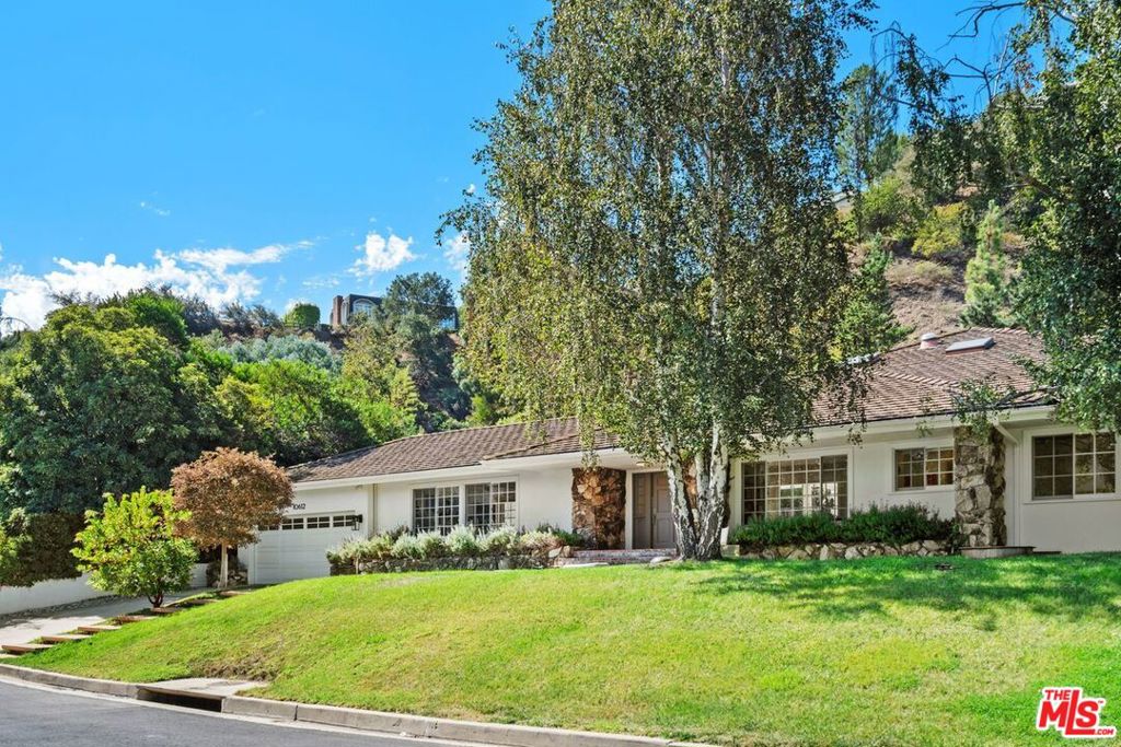 Nestled in a private cul-de-sac off prestigious Stone Canyon Road in Bel Air, this 5-bedroom, 4-bath California Traditional residence embodies timeless elegance with modern comfort. From the moment you step into the wide foyer, walls of windows flood the home with natural light and frame serene views of lush greenery and a sparkling pool. The expansive living room impresses with soaring ceilings and an airy, open feel, while the dining room provides an intimate setting overlooking the beautifully landscaped front yard. The gourmet kitchen is a chef's dream, featuring marble countertops, a Sub-Zero refrigerator, Waterworks fixtures, a large center island, and wraparound windows that bathe the space in sunlight. A spacious dining area by the fireplace looks out to the backyard, creating the perfect spot for gatherings and entertaining. The main level offers four bedrooms, including a wing with three bright, generously sized skylit bedrooms and a beautifully appointed bathroom, plus an additional en-suite bedroom with direct access to the backyard lounge area. Upstairs, the primary suite is a secluded retreat, offering a large bedroom overlooking the pool and gardens, a beverage/coffee bar, a sizable walk-in closet, and a spa-like bathroom with dual vanities, a skylight, and a glass-enclosed shower. The outdoor spaces are designed for both relaxation and entertaining, with mature landscaping, a sparkling pool, outdoor kitchen, covered terrace, and multiple seating areas ideal for al fresco dining. A two-car garage comfortably fits two SUVs. A rare gem in one of Los Angeles' most exclusive neighborhoods, this remarkable home must be seen to be fully appreciated.