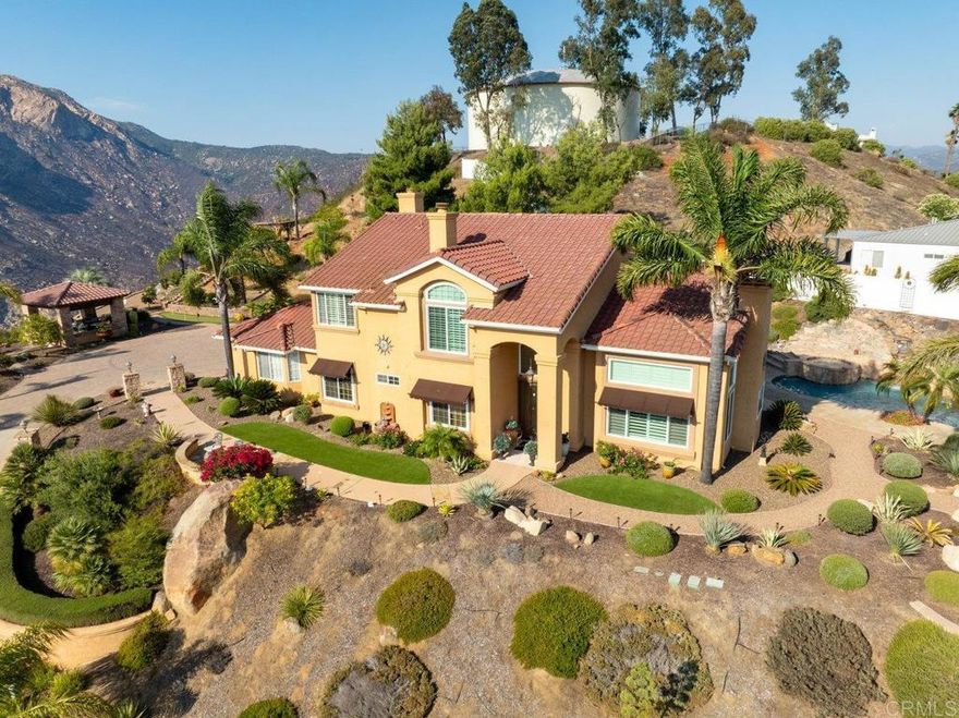 Perched atop a serene hillside in Blossom Valley, this extraordinary estate offers a private resort lifestyle with sweeping westerly vistas and sunsets that paint the sky in an ever-changing masterpiece. Set on a meticulously landscaped 3-acre lot, the residence spares no detail in design or craftsmanship. A paver-lined drive with circular entry and pillar lighting leads to the stately façade and 3-car garage.  Inside, the home blends elegance and comfort. The main level features a full bedroom and bath, executive office, and formal living and family rooms, each with a fireplace. The gourmet kitchen flows into the dining area and out to a covered patio through accordion glass doors, creating seamless indoor-outdoor living perfect for intimate dinners or poolside gatherings.  The backyard is a sanctuary of relaxation and fun—grill and dine alfresco, enjoy tranquil water features, swim in the shimmering pool, or unwind in the spa, both illuminated at night for a magical ambience. Harvest fruit from your orchard or practice on your private canyon-view putting green.  Upstairs, the primary suite is a retreat of its own with a sitting area and double-sided fireplace. The spa-inspired bath includes a cedar-lined walk-in closet, dual vanities, oversized shower, and deep soaking tub.  Additional amenities include a well-appointed laundry room with storage and folding space, lush mature landscaping, and the crisp mountain breezes that make this home so uniquely desirable. If sweeping views, refined luxury, and total privacy are on your list, this mountaintop gem awaits.