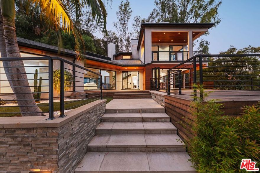 Nestled in the tranquil hills of Studio City, this 5-bedroom, 6-bath residence offers privacy, abundant natural light, and canyon views. Walls of glass and folding doors create a seamless indoor-outdoor flow throughout the expansive living spaces. The interiors combine warm wood accents, sleek black finishes, and polished concrete floors balanced by a soft, neutral color palette.The upstairs primary suite is a retreat of its own, highlighted by soaring ceilings, a stone fireplace, private viewing balcony, and spa-like bathroom with dual vanities, a jacuzzi tub, walk-in shower, and skylight. Secondary bedrooms are generously sized, while a versatile lounge/library provides an ideal bonus space.Outdoor living is elevated by wraparound decks, multiple seating areas, and terraced pathways that lead to a hillside retreat and lookout point. Peaceful yet accessible, this property is just minutes from Ventura Blvd's shops and restaurants, with convenient routes to the Westside and beyond.