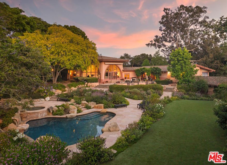 Positioned behind gates in the coveted enclave of Hope Ranch, this residence spans approximately 1.94 acres of beautifully landscaped grounds, offering timeless sophistication and exceptional comfort. The 6-bedroom residence includes two primary suites and an array of thoughtfully designed living spaces ideal for both relaxation and entertaining. Upon entry, the living room immediately commands attention as the focal point of the home, featuring soaring ceilings, a statement chandelier, and a striking fireplace. Large doors open to a grand stone terrace overlooking a cascading waterfall pool, lush gardens, and an expansive lawn - creating a seamless flow between indoor and outdoor living.A distinctive dining room connected directly to the kitchen offers captivating views of the backyard and effortless flow for gatherings. Just off the main living areas, a stylish den with a built-in bar offers the perfect setting for entertaining. Step outside the den's doors to discover a built-in fireplace with wraparound seating, ideal for intimate evenings under the stars. The primary suite is a serene retreat with a beautifully crafted fireplace and expansive windows that frame views of the surrounding landscape. The 3-car garage includes a temperature-controlled room for wine storage - an ideal amenity for collectors. Access to Hope Ranch's exclusive offerings, including private beach access, scenic riding trails, and tennis courts, further elevates this extraordinary lifestyle. Completing the estate is a beautifully designed 2-bedroom, 2-bath Accessory Dwelling Unit, built just over two years ago with its own driveway and address, offering stylish, self-contained accommodations with privacy and flexibility.
