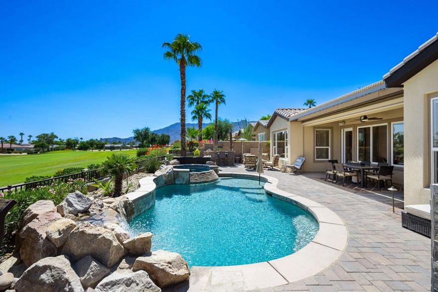 This elegant single-level Anise design Solar home in the prestigious Trilogy community offers stunning views along the #5 fairway of the golf course, with mountains and desert as the backdrop. The private oasis's backyard features a Pebble-Tec pool, cascading spa, rock waterfall, BBQ island with bar seating, a paver deck, and a covered patio with outdoor speakers, misters and up-lighted landscaping. The 3-bedroom, 3.5-bath residence includes a versatile office/den, formal dining room, and a bright great room with a built-in entertainment center, surround sound, and remote-controlled shades. The gourmet kitchen boasts granite countertops, a prep island with bar seating, custom backsplash, and premium stainless-steel appliances, with thoughtful touches like pull-out shelves and under-cabinet lighting. The luxurious primary suite offers a serene sitting area, dual vanities, upgraded marble finishes, and a walk-out patio. Additional highlights include custom built-ins, full-house LED lighting, remote-controlled shades, an outdoor drop shade, an etched glass front door, and an epoxy-floored 2-car extended garage with room for a golf cart and built-in storage. This home near the Santa Rosa Clubhouse provides easy access to Trilogy's world-class amenities. Experience the ultimate resort-style desert living.