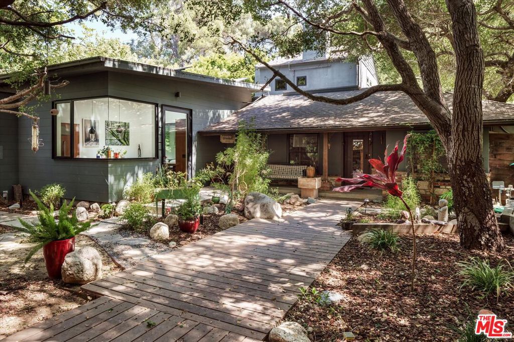 Set on a sprawling, gated, flat lot of approximately 10,000 sf, beneath a canopy of mature oak trees, this quintessential 1940s California Ranch-style home seamlessly blends classic canyon charm with a thoughtful 1100sf+ modern kitchen addition, completed in 2017. The original home is still intact, with vintage details like wood beams, flagstone fireplace mantel and Laurel Canyon vibes for days. With 4 bedrooms, 3.5 baths, and multiple flexible living spaces, this is a one-of-a-kind extraordinarily emotional property that is suitable for anyone in search of envisioning and manifesting their own creative compound. A striking, light-filled kitchen addition serves as the heart of the home built for large or intimate gatherings - an entertainers dream - and features soaring ceilings, clerestory and corner-less windows, Fleetwood doors to the outside spaces, premium appliances, custom cabinetry and an oversized island. There is a bedroom/guest room/office adjacent to the kitchen, with bathroom, that can be used for any number of purposes. The house reads like a classic single story home, with the exception of the primary bedroom suite. Occupying the upper level, it is a private retreat, complete with an ensuite bath, walk-in closet, balcony overlooking the yard and and sweeping treetop views. The additional bedrooms are located on the main level, along with a den an office and a studio with side entrance and access to the back yard space (with room for pool) - suitable for media room, recording or rehearsal, gym, production space and more. Outdoors, the sprawling, flat lot offers exceptional potential with multiple nooks and moments - and the serenity of heritage California oak trees creating a rare sense of privacy and possibility. There is a 2 car garage inside the gates of the property, a separate carport and additional private, off street parking for multiple cars. This is Canyon Living at its best, indoor outdoor living with true connection to nature. Bring your architect or designer to make some upgrades to the original portion of the structure and you have a dream homestead for the ages - walking distance to Wonderland School - private and serene, with room for all your friends and family to come and make memories.