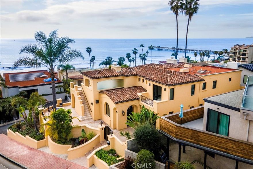 Just two homes from the ocean, this custom estate by architect Michael Luna showcases architectural refinement, superior craftsmanship, and coastal luxury. Engineered for longevity, it is supported by 42 caissons, ensuring a lasting foundation atop its coveted location. Overlooking T-Street Beach and the scenic beach trail, it offers breathtaking, unobstructed views of the Pacific, Catalina Island, and the San Clemente Pier—a front-row seat to golden sunsets and rolling waves. Beyond its gated entry, a travertine courtyard introduces the stately façade, where handcrafted ironwork, arched doorways, and Mediterranean details evoke timeless elegance. Inside, soaring ceilings, travertine flooring, and curated stonework are bathed in natural light from expansive windows and French doors. Designed to maximize panoramic views, this 4,035 square foot residence seamlessly blends indoor sophistication with exceptional outdoor living. Multiple ocean-facing terraces, both covered and open-air, offer a coastal experience from sunrise to sunset. The great room, anchored by a statement fireplace, extends onto a covered balcony with a fireplace and lounge seating, creating a tranquil retreat with endless ocean vistas. A separate terrace provides sunlit spaces for al fresco dining or unwinding to the sound of waves. At the heart of the home, the gourmet kitchen is a culinary haven featuring top-tier appliances, an oversized island, and custom cabinetry. Designed for effortless entertaining, it flows into the dining area and outdoor terraces, where ocean views create an unforgettable ambiance. Each of the five en-suite bedrooms is a private retreat showcasing bespoke finishes, custom millwork, and spa-like baths. The primary suite is the pinnacle of indulgence, positioned to capture sweeping ocean vistas. Step onto your private balcony, where salt air and rolling waves provide a serene escape. The spa-inspired bath features a soaking tub, steam shower, dual vanities, and a walk-in closet with custom built-ins. Amenities include a built-in surround sound system, dumbwaiter, whole house water filtration and three-car garage, ensuring comfort and convenience. Thoughtfully designed for coastal luxury, this residence is more than a home—it’s a sanctuary where indoor and outdoor spaces harmonize with the Pacific. Moments from San Clemente’s pier, Historic Del Mar, and miles of recreation, this estate is a rare opportunity to own a premier piece of California’s coastline.