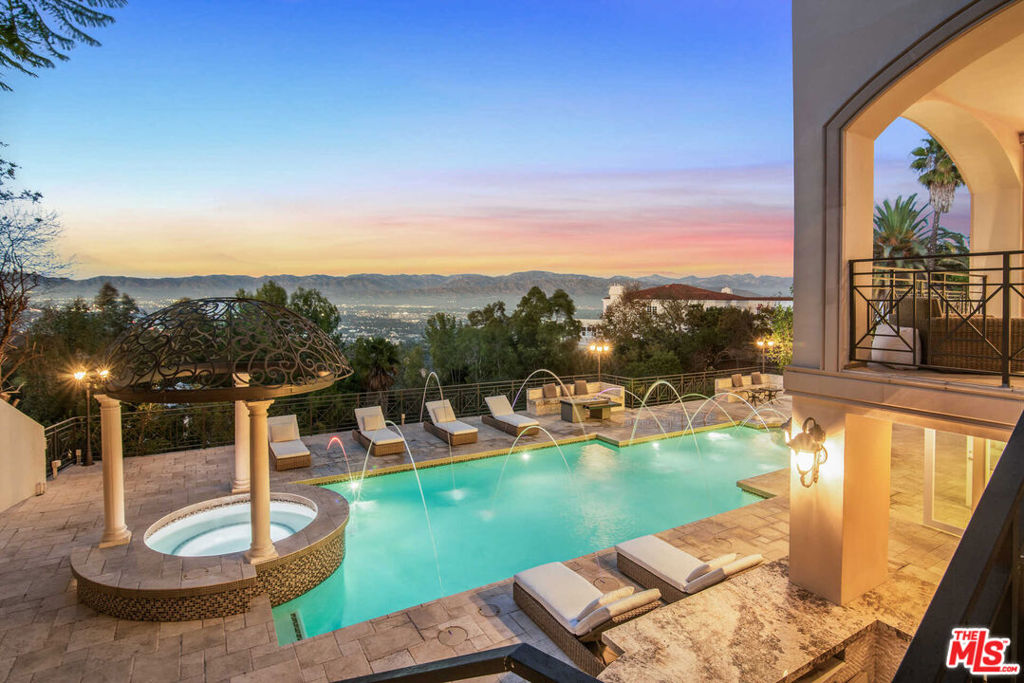 Nestled within The Summit, an exclusive gated community along Mulholland Drive, resides 12063 Crest Court, offering unparalleled vistas in the prestigious Beverly Hills zip code. Spanning three levels, this refined sanctuary boasts six bedrooms and seven bathrooms, inviting you to curate the life you've envisioned within its expansive confines, accentuated by lavish panoramas. Beyond the home's wrought iron fence lies a lush oasis, with meticulously landscaped greenery setting the scene. The exterior showcases a striking red-tiled roof, illuminating outdoor sconces, and a grand entrance. Step inside to discover a foyer adorned with a resplendent Christopher Guy chandelier, a gracefully curved staircase, and pristine white tile floors, suffusing the space with an air of opulence. The formal dining room exudes elegance with its silver-plated Bisazza tile and lofty windows framing breathtaking canyon and city views, seamlessly flowing into a stunning living area featuring a fireplace and intricate gold-plated Bisazza tile wall mosaics, with a balcony accessible through three sets of French doors.The chef's kitchen is a culinary masterpiece, boasting a backlit marble island and countertops, sleek glass cabinetry, a cozy dining nook, top-of-the-line SubZero refrigerator, Wolf range, and Miele coffee machine. Elevating the experience, a wine cellar, Swarovski crystal light fixtures, and an elevator add to the allure. The primary suite is a sanctuary of serenity, prioritizing panoramic views, while each additional bedroom exudes its own unique charm. Outside, a multi-tiered paradise awaits, featuring a saltwater pool adorned with vibrant colored lights, a rejuvenating spa, and two inviting fire pits. Completing the picture-perfect retreat is a sauna, offering the ultimate at-home spa experience. With a spacious 3-car garage and the finest amenities of Beverly Hills mere moments away, this residence seamlessly combines privacy with convenience, epitomizing a lifestyle of unparalleled luxury and tranquility.