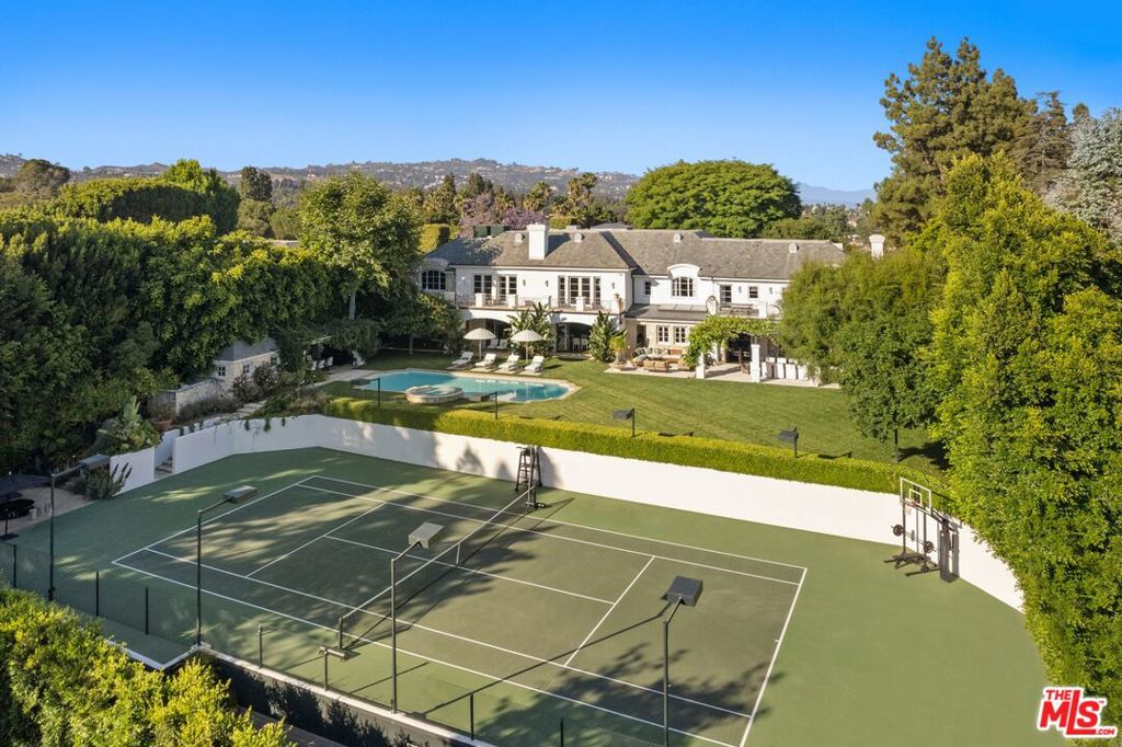 Set beside the exclusive LA Country Club, this expansive 1-acre gated estate has been meticulously remodeled to blend old-world glamour with modern elegance. Set back behind a grand, gated motor court, the property ensures unparalleled security and privacy. A grand two-story foyer with warm tones, natural light, and graceful curved lines creates an inviting and sophisticated atmosphere. To the right, a formal living room with a fireplace sets the stage for elegant entertaining, while an office with a bar and coffered ceiling adds timeless charm. Multiple gathering spaces, including a dining room overlooking the manicured grounds, flow seamlessly throughout. The opposite wing features a gourmet kitchen with dual islands and top-of-the-line appliances, a breakfast nook, and a cozy family room that opens to an outdoor dining area shaded by mature grapevines. Upstairs, the expansive primary suite features a fireplace, dual walk-in closets and bathrooms, and a private balcony overlooking the backyard and golf course. Five additional bedroom suites offer ample space for family and guests. Outside, a private oasis awaits. Lush landscaping surrounds a large patio for dining al fresco, firepit, flat grassy lawn, resort-like pool with spa, pool house with additional patio space, tennis court with lights, and an additional deck area that overlooks the impeccably landscaped fifth fairway. Offering a seamless blend of luxurious living and resort-style amenities, this estate provides an unparalleled opportunity to experience the epitome of refined elegance in one of Los Angeles' most coveted locations.