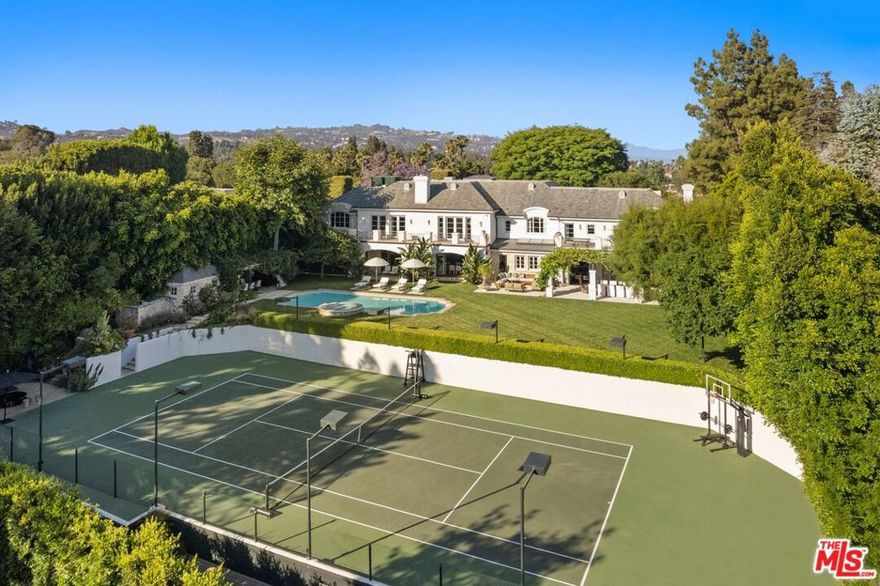 Set beside the exclusive LA Country Club, this expansive 1-acre gated estate has been meticulously remodeled to blend old-world glamour with modern elegance. Set back behind a grand, gated motor court, the property ensures unparalleled security and privacy. A grand two-story foyer with warm tones, natural light, and graceful curved lines creates an inviting and sophisticated atmosphere. To the right, a formal living room with a fireplace sets the stage for elegant entertaining, while an office with a bar and coffered ceiling adds timeless charm. Multiple gathering spaces, including a dining room overlooking the manicured grounds, flow seamlessly throughout. The opposite wing features a gourmet kitchen with dual islands and top-of-the-line appliances, a breakfast nook, and a cozy family room that opens to an outdoor dining area shaded by mature grapevines. Upstairs, the expansive primary suite features a fireplace, dual walk-in closets and bathrooms, and a private balcony overlooking the backyard and golf course. Five additional bedroom suites offer ample space for family and guests. Outside, a private oasis awaits. Lush landscaping surrounds a large patio for dining al fresco, firepit, flat grassy lawn, resort-like pool with spa, pool house with additional patio space, tennis court with lights, and an additional deck area that overlooks the impeccably landscaped fifth fairway. Offering a seamless blend of luxurious living and resort-style amenities, this estate provides an unparalleled opportunity to experience the epitome of refined elegance in one of Los Angeles' most coveted locations.