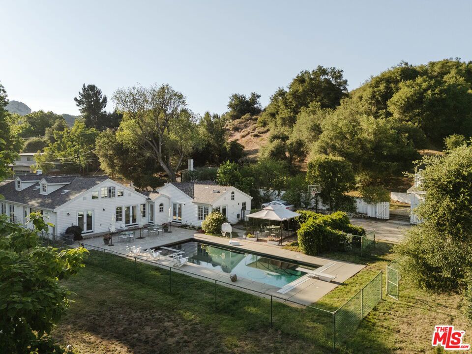 Own a Topanga Landmark, with 3 Homes on 2 Lots! At the far end of the Historic Bonnell Park, a storied New England style compound is set in lush, verdant, meadows, framed by towering oaks, cottonwood, maple, and ash trees. With the park serving as a de facto front yard, the white house with inky black shutters sits behind a long, flower-framed, white picket fencebeckoning as if from a bygone era. The cluster of 3 homes, encompassing the entire end of the Bonnell Cul de sac, harkens to farm country, with the main house sitting on over 1 1/3 acre of flat lawns and gardens. The two smaller cottages, each in a private, fenced yard, sit on a separate, adjoining 1/4 acre lot. Strawberry peak and Little Rock, two local icons, serve as a backdrop to this home. The history of Topanga is told here. The homes were once part of the original John Bonnell estate which includes "The Old Stone House"considered the oldest house in Topanga, built by Jack Wood, a pioneer stage and Post Office mail driver. They have been owned by just 2 families over the past 70 years, and were reimagined by Topanga's renowned architect, Cary Gepner, into the graceful sanctuary they are today. The brief was to seamlessly meld the indoors and out, so every room took in the beauty of the incredible grounds. He delivered. Rooms flooded with abundant natural light, encompass the perfect flow for celebrations, or quiet enjoyment. Visitors to the park often exclaim it is the "most beautiful home in Topanga!" Now is your chance to own this lyrical property, with its saltwater pool and spa, fruit trees, and gardens, all set along the banks of Old Topanga Creek. Over the years, this home has been cast as an East Coast home in movies and tv shows, because it calls nostalgically to us of simpler times. But the interiors are updated with serenely minimal rooms perfect for modern country living. Bare feet pad across polished old oak floors. The front foyer opens to a gracious, soaring, two story living room, with a classic fireplace. A wall of French doors looks out from the living room and spacious dining room to where deer meander, and hawksfloat on updrafts. The inviting open kitchen, with its vast island, hosts a crowd. Doors flung open to the huge patio, pool and spa, allow for that quintessential California indooroutdoor life! The spacious primary suite opens to the pool through French doors. Its bright bath, with a steam shower, vintage fixtures and a clawfoot tub opens to a poolside shower. Two other bedrooms with sun-splashed windows sit on the main level. A captivating suite of rooms under the eaves include an antechamber under automatic, venting skylights, that is perfect for reading or drawing. A small nook nearby entices as a hideaway play room. The bedroom up here is a fantasy space ripped from a classic tale, with windows overlooking the estate. The endearing one bedroom cottages share the same bright, pristine spirit as the main house, each with a fireplace. This home has an old soul, but a youthful spirit. Classical landscaping, with abundant flowers, bowers of roses, and trees laden with fruit surround the homes. Birdsong brightens your mornings, and frogs, crickets, and the soft hoot of owls serenade you at night. A chicken coop awaits hens. Protected Bonnell Park, Topanga's Halloween destination, is owned by a neighborhood association, and development of the park is forbidden. Red Rock State Park, Summit to Summit, and Backbone hiking trails are nearby. Topanga's cafes, shops, and cultural landmarks are close by. Malibu's fabled beaches are near enough to feel the coastal breezes. Hop to the 101 or the westside. You can have your rural dreams, and your big city life, too. The magic of this home abides, with shooting stars, darting bats, and the burble of the creek. And now you can weave your life into the sweet tale of this storybook home.