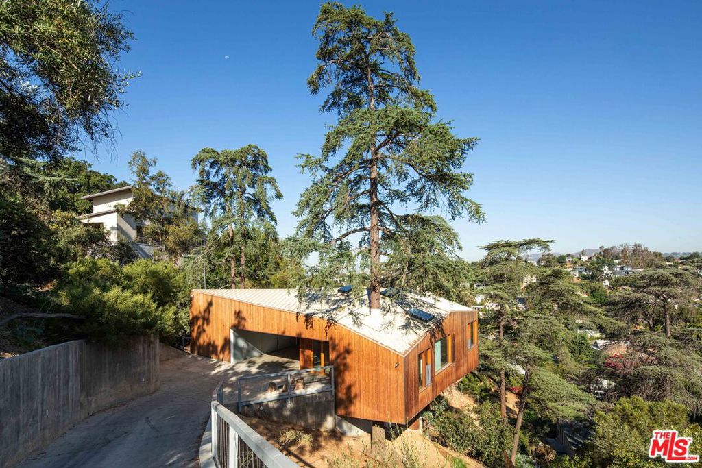 A striking architectural by Simon Storey of Anonymous Architects, the "House in Trees" is a one-of-a-kind residence that embodies Echo Park's creative spirit. Designed around a massive tree that rises through the center of the home, this 3BD/2BA, retreat offers the rare experience of modern design in harmony with nature.Set on a steep hillside among towering cedars, the minimalist form cantilevers over the slope with reclaimed cedar siding, and an undulating roofline that mirrors the terrain. Inside, expansive retractable glass walls, floor-to-ceiling windows, and wood-clad breezeways fill the spaces with natural light and canyon views. Custom details include reclaimed chestnut floors, a handcrafted bookshelf staircase to a lofted play space, and vintage hand-blown lighting.The chef's kitchen features handmade tile, warm wood cabinetry, and premium appliances, opening seamlessly to indoor/outdoor living areas. The primary suite is a sanctuary with a sunken soaking tub, steam shower, and serene canyon outlooks. Two levels of cantilevered decks extend the living experience into the treetops, perfect for entertaining or quiet reflection.Sustainable touches include a solar hot water heater and an EV charger in the garage. Located moments from the best of Echo Park yet secluded among the trees, this home offers a grown-up treehouse lifestyle rarely available for lease.