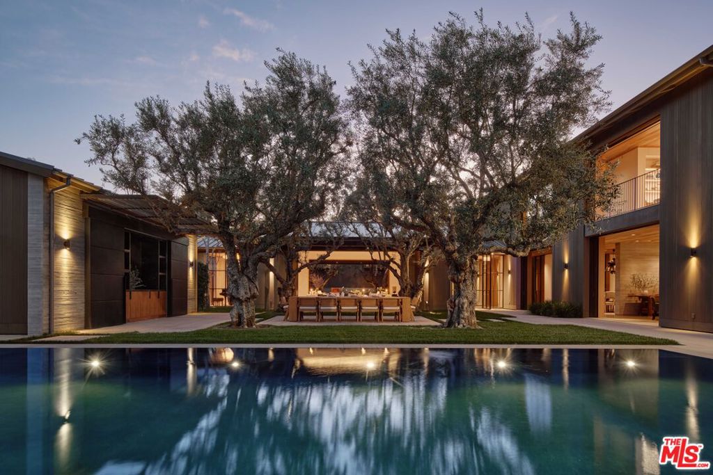 Just moments from the vibrant heart of Beverly Hills, Villa Oliva offers a serene escape that captures the essence of Napa Valley. This architectural gem, designed by Howard Backen, with landscapes by Mark Rios and interiors by Tommy Clements, blends nature with urban sophistication. Behind elegant gates, the refined facade features cedar wood, sleek concrete, and expansive glass. Enter through a stunning glass-walled bridge into a tranquil courtyard, showcasing exceptional craftsmanship and seamless indoor-outdoor living. The inviting spaces highlight natural materials and a fluid layout. The formal living room boasts a vaulted ceiling and pocket doors that frame picturesque views. Outdoor amenities include a chef's kitchen, alfresco dining area, a tennis court, and an infinity-edge pool, creating a resort-like atmosphere. The primary suite offers a peaceful retreat with a vaulted ceiling and doors opening to lush grounds, while the spa-like bathroom features marble finishes and dual walk-in closets. The lower level includes a wine cellar, billiard room, theater, and fitness studio. Villa Oliva is a unique sanctuary where architectural artistry meets nature, offering an unparalleled lifestyle for those seeking elegance and tranquility.