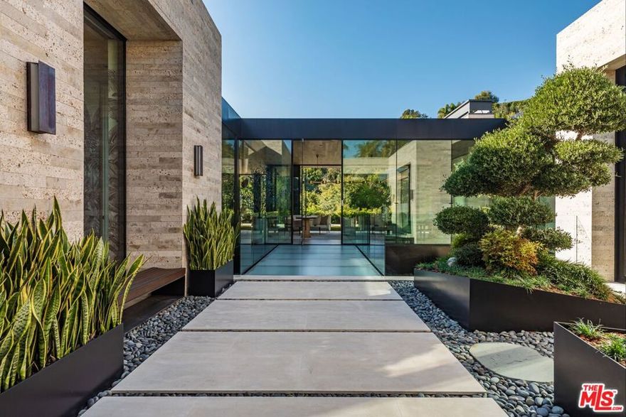 Discover world-class design and luxury in this organic contemporary Trousdale masterpiece crafted by award-winning architect Paul McClean and designer Lindsay Chambers and reimagined by Nate Berkus & Jeremiah Brent. Set on a prestigious, quiet cul-de-sac, this 11,000 SF home boasts an architectural exterior with custom Italian stonework. Mid-century-inspired steel grillwork surround the front door that opens to a showstopping glass bridge entrance. The two-story courtyard and walls of glass allow sunlight to fill the home and highlight the beautiful oak ceilings and Travertine walls. Glass walls open to a spectacular outdoor space featuring an expansive infinity pool with city and ocean views and a tranquil Japanese garden. The primary suite sits beside the pool as if it's floating above the water and offers a custom walk-in closet, and spa-like bathroom. Rejuvenate in the marble-clad indoor wellness center with hot and cold plunge, cedar sauna, and gym. Additional amenities include a stunning Nero Marquina-clad bar, home theater, subterranean auto gallery, and fairytale pink playroom. This architecturally significant home is a rare offering, even among the most discerning tastemakers in the city.