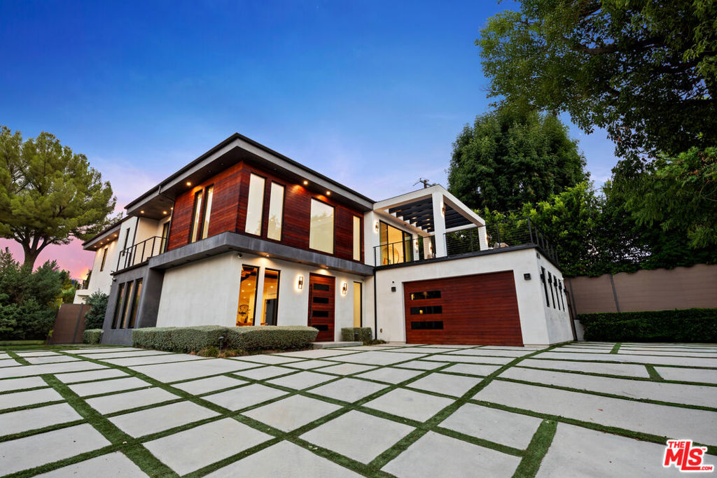 Ideally situated just off Ventura Boulevard, this striking modern residence blends transitional architecture with a flawless fusion of smooth stucco, rich exotic wood, and expansive glass walls all privately nestled behind lush hedges in a tranquil South of the Boulevard enclave. Step into a dramatic entryway with soaring ceilings, setting the tone for the thoughtfully curated interiors where open-concept living flows seamlessly into the outdoors. Beyond the foyer, a sophisticated formal living room with custom built-ins leads to a state-of-the-art home theater perfect for movie nights or game day gatherings. On the main level, a private guest or maid's suite with an en-suite bath adds flexibility, alongside a stylish powder room for visitors. The elegant formal dining room connects effortlessly to a warm and inviting family room, complete with designer built-ins, a 100-bottle wine bar, a contemporary wood-clad fireplace, and expansive glass pocket doors that disappear to reveal the breathtaking backyard oasis. The chef's kitchen is a showstopper, outfitted with a waterfall island, sleek lacquer cabinetry, premium built-in Miele appliances, a sunny breakfast nook overlooking the grounds, and a walk-in pantry. A butler's pantry provides convenient access to the dining room ideal for entertaining with ease. Upstairs, a versatile teen lounge or executive office opens to an extraordinary wraparound terrace with panoramic views of the Santa Susana Mountains. Four luxurious bedroom suites await, including a spectacular primary retreat featuring a fireplace, built-in bar and fridge, private lounge, oversized walk-in closet with island, and a spa-inspired bathroom with dual vanities, lighted mirror, soaking tub, and oversized shower. A private balcony overlooks the backyard the perfect spot to greet the morning or unwind at sunset. Designed for entertaining and everyday luxury, the backyard features a covered outdoor living area, sparkling pool and spa, glass-encased fire pit, and a sleek outdoor kitchen with built-in BBQ. A custom sports court invites friendly competition, while a newly updated ADU with a private entrance and en-suite bath provides ideal accommodations for guests, extended family, or use as an office, studio or even a gym. Smart home features include integrated sound, multi-zone Nest climate control, security cameras, electric blinds and curtains throughout the entire house and full home automation. Additional highlights include a large motor court with ample parking and a low-maintenance turf area perfect for soccer, mini golf, or outdoor relaxation. Don't miss the opportunity to experience the exceptional lifestyle offered at 4854 Alonzo Avenue where modern design, comfort, and convenience converge in one unforgettable home.