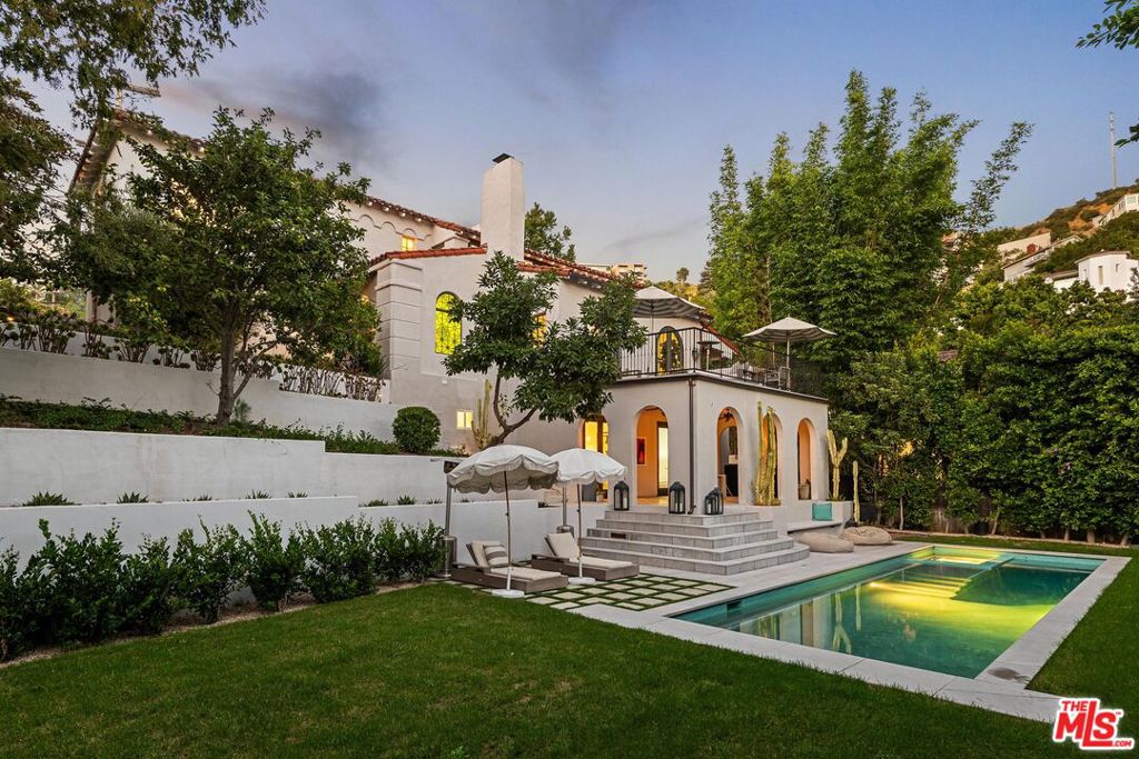 Perched in the coveted Hollywood Hills, this stunning Spanish-inspired estate masterfully blends old-world charm with modern sophistication. Tucked behind private gates and lush greenery, the home exudes character with its stained glass accents, hand-painted Spanish tiles, and intricate wrought iron details. Step inside to be greeted by a striking stained-glass window and exquisite tilework, setting a refined yet inviting tone. The main level features a grand living room with a fireplace, seamlessly extending to two patios that showcase breathtaking city views. A formal dining room and a chef's kitchen, complete with marble countertops, a spacious walk-in pantry, and a wine fridge, offer an ideal setting for hosting. Illuminated by bespoke Murano glass chandeliers and designer lighting from Soho Homes & Allied Maker, the residence radiates elegance throughout. The lower level is home to a custom screening room that opens to a charming loggia, leading directly to an outdoor sanctuary. The beautifully reimagined gardens by acclaimed designer GSSM frame a sparkling pool, spa, and manicured lawn, all enhanced with smart irrigation technology for effortless maintenance. With five bedrooms and four and a half bathrooms, this home provides a perfect balance of luxury and comfort. Behind the gated driveway, five-car parking adds convenience, including an attached two-car garageone thoughtfully converted into a state-of-the-art private gym, complete with cutting-edge equipment and an oversized LED-lit custom mirror. Positioned just moments from the Sunset Strip, this exceptional property captures the essence of Hollywood Hills living, offering a private retreat with sweeping views and a seamless indoor-outdoor flow.