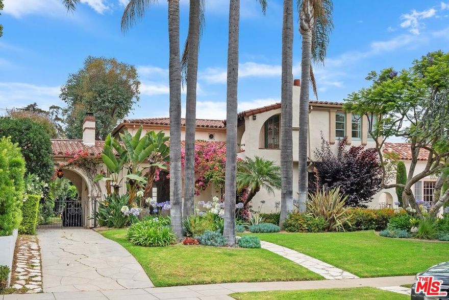 Perched on a knoll surrounded by majestic palm trees, this stunning two-story Spanish Colonial Revival home, built in 1928, is located in the desirable area of Gillette's Regent Square. The residence features three bedrooms and two and a half bathrooms, as well as a spacious family room that overlooks the beautifully landscaped garden. Upon entering, you'll find yourself in a tiled vestibule that leads to an exquisite formal living room characterized by soaring wood-beamed ceilings, a wood-burning fireplace, and leaded glass windows. This unique home retains the charm and character of the 1920s, highlighted by arched doorways, wrought iron handrails and doorknobs, scalloped stair steps, and authentic period details. The expansive kitchen boasts quartz countertops, ample cabinetry, a cozy home office, and an inviting breakfast room. The large formal dining room features a barrel ceiling adorned with rope molding, providing a perfect space for gatherings. Upstairs, you'll discover a generous primary suite complete with an original tile bathroom, a delightful balcony, and a cedar-lined walk-in closet, along with two additional spacious bedrooms, each featuring walk-in closets. The lovely full bathroom showcases a unique cylindrical shower stall adorned with period tilework from the 1920s. The converted garage serves as valuable storage space adjacent to a bonus room with a quarter bath and a separate laundry room, offering potential for an ADU (Accessory Dwelling Unit). The mature, landscaped backyard is home to olive, lemon, and tangerine trees, and features a wisteria-covered pergola over a tiled patio, a fountain, and a trumpet vine-covered play stage for children, making it ideal for entertaining. There is also a porte-cochere providing covered parking, complete with an EV charger. This is a perfect opportunity to embrace the California lifestyle North of Montana Avenue.