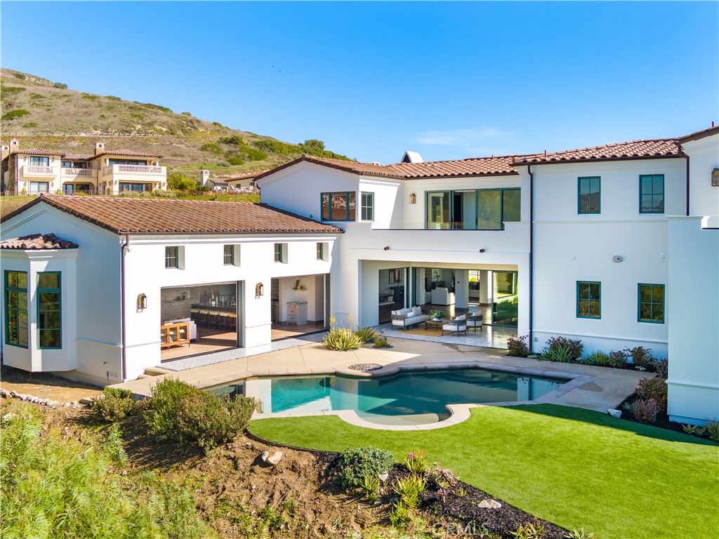 This 2019-built Spanish-style masterpiece is situated in the prestigious coastal enclave of The Estates at Trump National Golf Course. Surrounded by scenic nature reserves and an award-winning golf course, this exceptional residence offers unmatched luxury and breathtaking views of the Pacific Ocean and Catalina Island. With 6 bedrooms, 6.5 bathrooms, and over 6,100 sq. ft. of thoughtfully designed living space, this home redefines coastal elegance.
Enter through a grand 12-foot wrought iron door by Pinky’s to a showstopping interior featuring a curved marble staircase, a glass-enclosed wine showcase and expansive dry bar, perfect for entertaining. The gourmet kitchen is a chef’s dream, with a massive leathered marble island, Thermador appliances, Italian Macassar Ebony cabinetry, and rose gold Brizo fixtures. Additional highlights include a butler’s pantry with a built-in coffee maker and a secondary dry bar. Soaring ceilings and luxurious finishes create an ambiance of coastal glamour and modern sophistication.
Seamless indoor-outdoor living defines the home, with four pocket sliding doors opening to a 375 sq. ft. covered California room, complete with a built-in BBQ and tiled flooring. The expansive backyard features a sparkling pool, spa, firepit, and lush landscaping, offering a private oasis for relaxation and entertaining. A detached guest suite with a private entry and bathroom adds versatility, ideal as a pool house, yoga studio, or office.
The primary suite is a true retreat, with oversized walk-in closets, sweeping ocean and Catalina views, and a spa-like bathroom featuring a marble shower with dual shower heads and a centerpiece soaking tub. Guest bedrooms include ensuite bathrooms, and many offer private balconies.
Additional features include an elevator, hand-selected light fixtures, dual-zone air conditioning, and a 3-car garage. Residents enjoy privileges at Trump National Golf Club, concierge services, and 24/7 security patrol, ensuring a lifestyle of convenience and peace of mind. This extraordinary estate embodies the pinnacle of California coastal living—don’t miss the opportunity to call it home