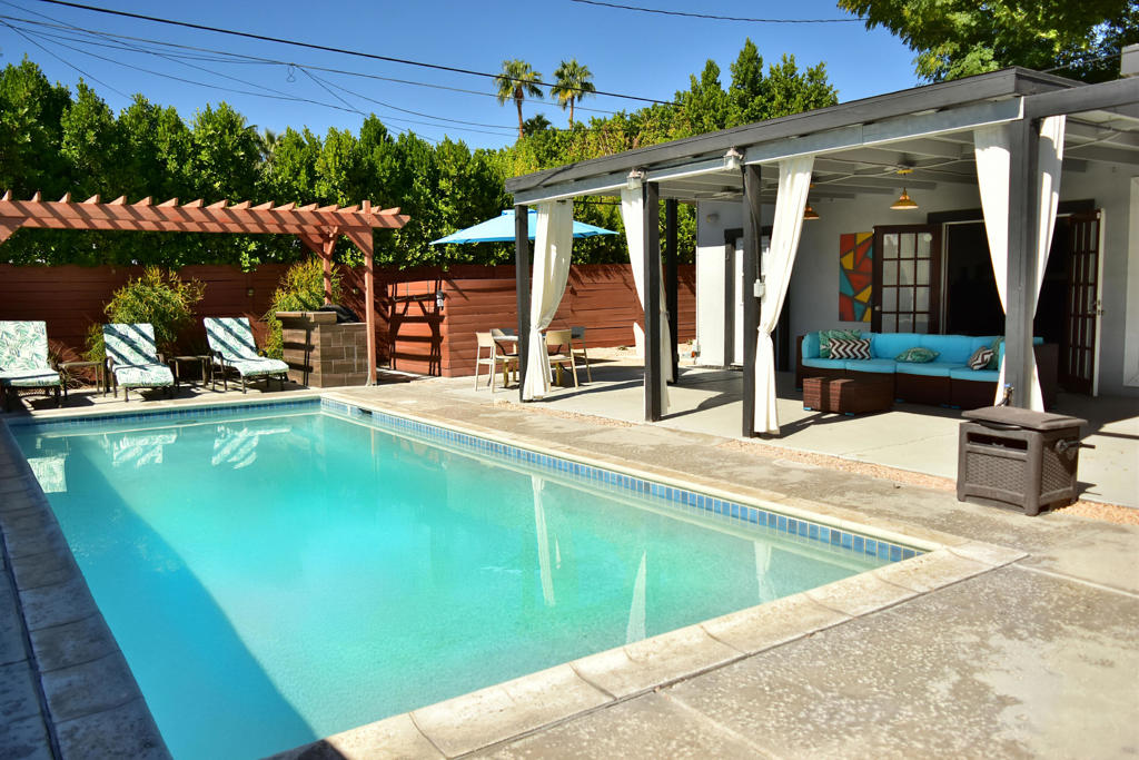 Make everyday a get-away in this charming MID-CENTURY Palm Springs home with popular Movie Colony East character and easy access to downtown. Enjoy leisurely days by the sparkling pool, perfectly positioned for maximum sun exposure and beautiful westerly mountain views. A pergola and cabana-style patio overhang create inviting spaces for relaxation. Ideal for full-time residency, weekend getaways, or seasonal escapes, the property has owned SOLAR and is very private with an enclosed front yard perfect for pets and family fun. There are also fruit trees and space for gardening enthusiasts. This 4-bedroom/2-bath home lives large with an updated open kitchen, breakfast bar, expansive dining/family room, and cozy living room with fireplace & French doors opening to the patio/pool area. The primary bedroom offers direct access to the pool/patio and to an updated bath. Three additional bedrooms and guest bath easily accommodate guests, with guest bath and 4th bedroom each opening directly to the pool/patio. Additional highlights include a one-car attached garage, separate laundry room, and tile & laminate flooring throughout. Furnishings available per inventory. This is THE essence of relaxed Palm Springs living. No HOA fees in this neighborhood.