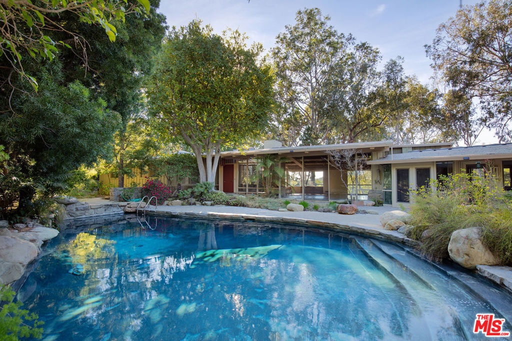 Poised on an awe-inspiring 1.4 acre, tree-filled promontory site affording great privacy and breathtaking canyon as well as distant ocean views, lies this sprawling 1950's Contemporary Ranch by much-admired early California architect Allen Siple. Set well off the street down a long, gated driveway in the estate section of Bonhill (just off of Tigertail), this magical property is set amidst towering trees and features over 200 feet of frontage with wrap-around views of the canyon with the Santa Monica Mountains and Pacific Ocean beyond. The centerpiece of the house is a fabulous "great room" with walls of glass and vaulted old-growth timber ceiling that opens to pool, terrace and front and rear gardens. All important rooms including the primary suite, kitchen, living, dining and two large offices take full advantage of the lush, gorgeous setting. Spacious upstairs room bounding with fabulous natural light has the flexibility to be a large bedroom or art studio/office. Surrounded by extraordinary major estates but with complete privacy, seclusion, tranquility and an out of Los Angeles feel, this property and its potential will captivate you from the moment you enter.