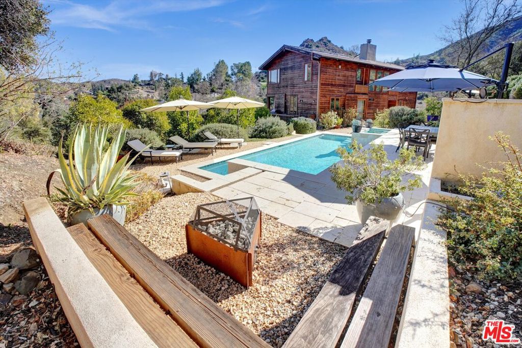 Contemporary mountain retreat above Malibou Lake available for lease unfurnished! Set on over 2.5 acres and surrounded by sweeping canyon and mountain views, this stylish home offers elevated living immersed in privacy and natural beauty. Warm and light-filled, the home features vaulted wood-beamed ceilings, expansive picture windows, custom architectural built-ins, rustic accents, and sliding glass doors that open to multiple decks - framing the landscape and inviting the outdoors in. The open-concept living space is anchored by a striking limestone fireplace and flows seamlessly into the dining area and chef's kitchen, complete with stainless steel appliances, bar seating, and abundant cabinetry. Designed for both relaxation and entertaining, the property boasts a sparkling pool and spa, media room, generous outdoor living spaces, and true farm-to-table living with raised garden beds, a greenhouse, fruit trees, berry bushes, and a chicken coop. There is also an attached bonus room on the lower level with separate access and a private patio that could be used as a large office, workout space, music room, and more. Additional highlights include solar, a detached garage, generous driveway parking, and close proximity to scenic hiking trails. Offering the perfect blend of seclusion and convenience, this exceptional home is just minutes from the 101 freeway and Malibu's sandy beaches. Available now unfurnished!