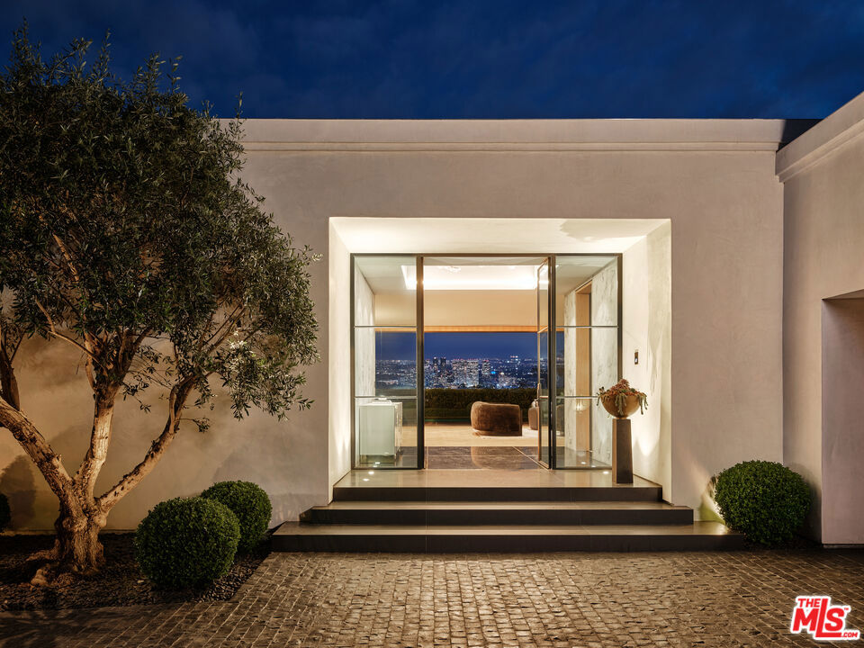 Pristinely positioned behind grand bipartite gates sits Trousdale Estates' most preeminent new-build residence. Welcome to 534 Chalette, where the designers and architects seamlessly blended Trousdale's three most coveted attributes into one sumptuous home: ultimate privacy, extraordinary build quality and dramatic skyline vignettes. Eight ancient Sevillano olive trees welcome you into the gated motor-court while Euroline steel case French doors lead you into the main home entrance. The bespoke crystal and hand-blown glass chandelier shines through the foyer skylight making for an incredibly dramatic entrance to the home, flanked by unobstructed skyline and ocean views in every direction. The custom kitchen was imagined by Molteni&C Creative Director Vincent Van Duysen in a sweeping open layout designed to maximize the room's natural light, creating a dialog between the outdoors and indoors. Cabinetry in black matte lacquer and lava stone countertop surfaces are complemented by bronze metal finishings for an ultra luxurious palette that seamlessly conceals bespoke Gaggenau appliances.The home's primary bedroom features dual separate bathrooms and walk-in closets crafted in larix dark wood with piqu drawers, bronze metal finishings and transparent glass doors. The closets are configured with 2 parallel sides offering an array of storage and a wall-length mirror on the far wall. The walls in the primary are lined with an intricate 505 system in glossy anthracite with dark brown leather shelving and glass sliding doors, offering customizable storage operated by remote control for books, a television, and miscellaneous personal effects.All additional bedrooms have custom onyx en-suite bathrooms and feature Euroline steel doors leading to the outdoors from every room. Additional amenities and features in this one-level compound include: a home theater, fitness center, sitting room with gorgeous bronze-built wet bar, designer wine cellar, and a nationally recognized glass blowing sculpture in Skylight called "Galaxy" by David Gappa, designed specifically for this property, and includes 400 individually blown glass orbs with clear, frosted and opalescent glazes. OVER $1,000,000 worth of furniture and art is also included in the purchase price. The acquisition of this custom estate is an opportunity not to be missed.