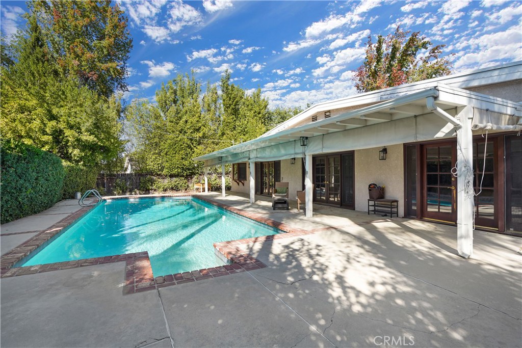 Exceptional single-story pool home located in prime Woodland Hills. A double wood door entry welcomes you into this spacious residence featuring high ceilings and wood flooring throughout. The formal living room with fireplace, formal dining room, and open family room all flow seamlessly to the backyard through three sets of French doors, creating the perfect indoor-outdoor living experience. The kitchen offers a garden window, breakfast area, and ample cabinet space. The primary suite includes French doors leading to the backyard, dual sinks, a soaking tub, and a separate shower. Large secondary bedrooms provide plenty of space and comfort. Lush landscaping in the backyard enhances privacy and complements the inviting covered patio and pool area. Additional highlights include a charming brick-inlay driveway, a thoughtfully designed floor plan ideal for entertaining, a newer roof and HVAC system, a beautifully resurfaced pool with updated tile work, and newly installed redwood fencing and side gate on the north side.