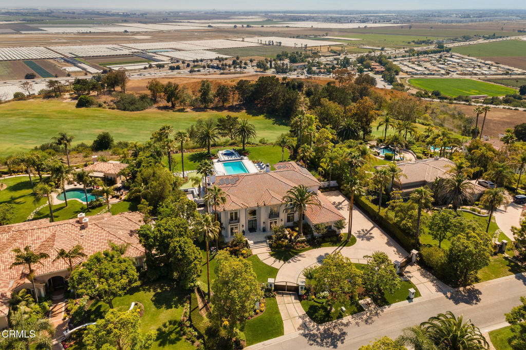 Tucked away in Camarillo's coveted Spanish Hills community and perched on the 15th fairway of the Spanish Hills Club, 1069 Corte Barroso sits on one of the best lots in the neighborhood. This grand 7,121 SF contemporary estate on a flat, lush 1-acre lot features 6 bedrooms, 6.5 bathrooms, and a fully gated entrance offering premier privacy and exclusivity. Panoramic golf course and ocean views elevate everyday living in this beautifully designed residence that blends rich textures, clean lines, and luxurious scale. A dramatic formal entry welcomes you into voluminous interiors, where a soaring great room with a stone fireplace and oversized windows creates an elegant yet inviting space for gathering. The fully renovated and expanded kitchen is a chef's dream, outfitted with paneled Sub-Zero and Asko appliances, Wolf double ovens, induction + gas cooktop, microwave, two warming drawers, a large island with breakfast bar, dining area, built-in desk, and separate scullery. Oversized windows and a wall of French doors frame the serene outdoor space, enhancing the seamless indoor-outdoor flow. Flanking the entry are formal living and dining rooms, while the true showpiece downstairs is a moody, speakeasy-style bar with mini fridges, ice machine, oversized wine fridge, and custom woodwork. The main level also includes a spacious primary suite, laundry room, and an additional bedroom converted into a stunning office with custom cabinetry. Upstairs, a second expansive primary suite offers a large sleeping area, sitting room, modern electric fireplace, and French doors that open to a private terrace with jaw-dropping 180-degree views of Camarillo, the golf course, airport, and the Channel Islands--where sunsets are a daily highlight. Three additional guest bedrooms upstairs each feature ensuite baths for optimal comfort. The entertainer's backyard features lush, meticulously landscaped grounds, a renovated pool and spa, covered patio with built-in speakers, TV lounge with fireplace, full outdoor kitchen, putting green, and separate fire pit area. With an oversized 3-car garage, Tesla wall, owned solar and water purification systems, RV parking, and a truly unbeatable location, this estate is a rare offering and an exceptional place to call home.