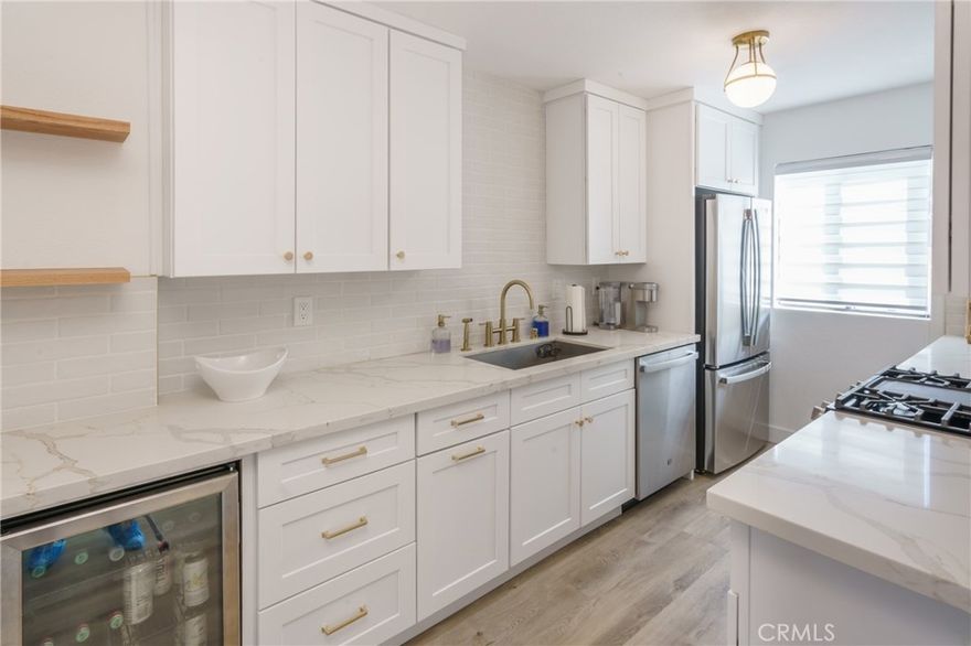 Stylish end-unit featuring a modern kitchen with quartz counters, white cabinetry, stainless GE appliances, and gold accents. Open floor plan with central AC/heat, LVT wood-look flooring, fresh paint, and updated doors/baseboards. Primary bedroom offers dual mirrored closets; guest suite with custom glass doors. Enjoy tree-top views from the balcony. Includes 2 secured tandem parking spaces with storage and elevator access. Prime Bixby Knolls location near shops, dining, parks, and easy freeway access.