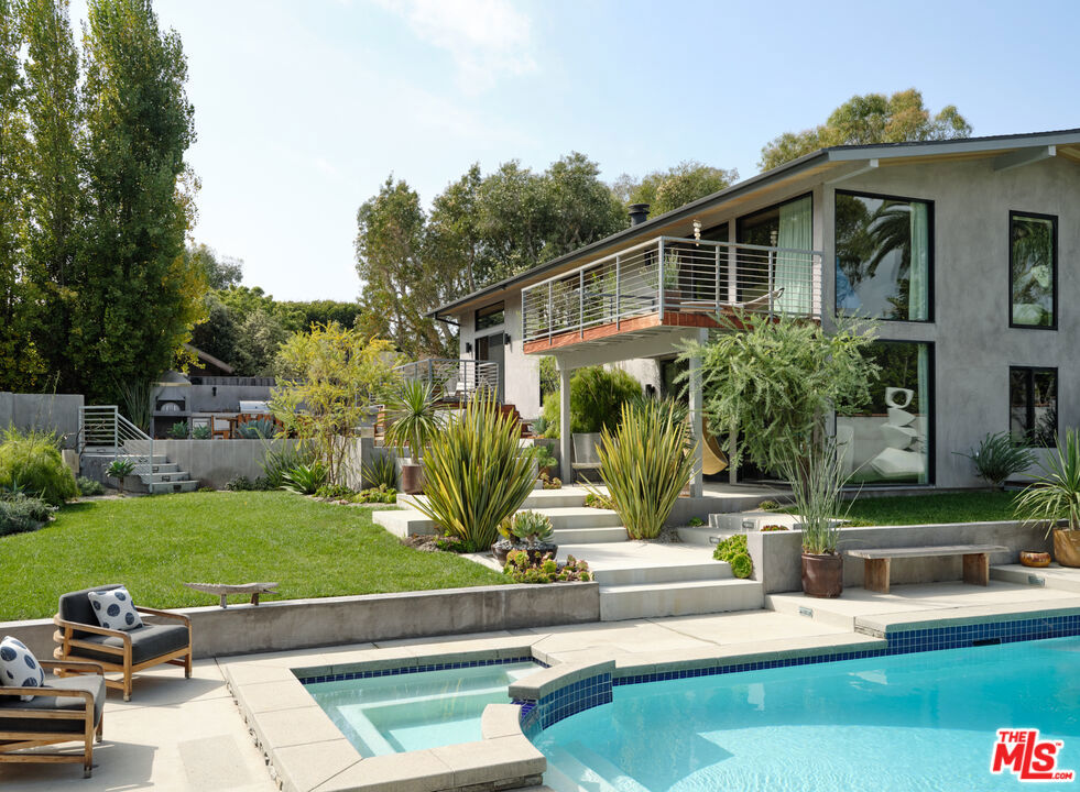 Gorgeously reimagined inside and out, this Point Dume residence has the atmosphere and amenities of a private resort, including a coveted Riviera 2 beach key. Complete with north-south tennis, pool and spa, sports court, outdoor kitchen, and manicured landscaping, this is indoor-outdoor living at its finest. Located behind gates at the end of a private drive, the all en-suite estate has an open, contemporary interior with high, plank-and-beam oak wood ceilings, skylights, art gallery walls, wood floors, and large windows and glass doors opening onto decks, patios, and gardens. The multi-level central living area features a spacious, step-down living room with double-height ceilings, a corner fireplace, and floor-to-ceiling glass with doors to the backyard. Four wide, floating wood steps lead up to the dining area, which features a fossilised stone wet bar, built-in cabinets, and a wall of glass opening onto a back deck. Along with the foyer, also on this level is the kitchen, a culinary masterpiece with beautiful fossilised honed stone countertops, a large island with bar seating, top-of-the-line appliances, and expansive walnut pantry cabinets. Off the entry, steps lead down to the den/media room, which has doors to both the front and back yards. A beautiful skylight office features a custom walnut live-edge built-in desk. The first of the home's five en-suite bedrooms is a bunk room, with four built-in oak bunks and a built-in desk. A half-flight up from the foyer is a hallway with two bedrooms, including the primary suite, which has wraparound windows, a private deck overlooking the backyard and pool, and a dramatic marble and heath tile skylight bath with a pool-view stone tub. Steps down from the living room are two more en-suite bedrooms, both opening to the backyard, one with a covered patio just outside. The property is open and yet exceedingly private. At the front of the house, where there is ample room for guest parking, there is an entry courtyard garden with two decks. The back of the property provides an appealing array of settings for entertaining, lounging, and recreation, including an outdoor kitchen with a pizza oven, Lynx barbecue, and adjacent al fresco dining area. Decks and a wide back lawn offer ideal spots for watching tennis, and the pool has a huge sun deck plus another large lawn that extends along the side of the house. The home's additional features include a powder room, a large laundry room, and a hidden surfboard storage under the deck. This serene and majestic residence is a private and luxurious enclave on ultra-desirable Point Dume.