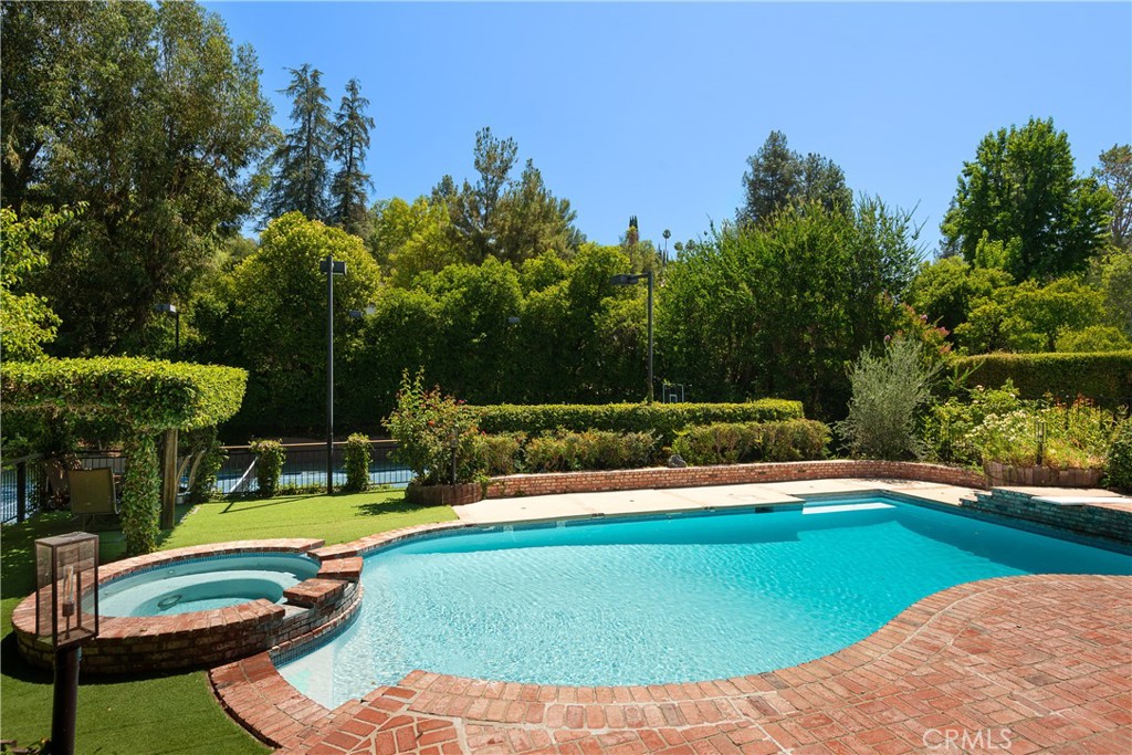 Privately situated behind secluded gates in one of Tarzana’s most sought-after neighborhoods just South of Ventura Boulevard, this timeless 1-acre tennis court estate is an exclusive sanctuary.
Two gates open to a long, treelined driveway and sprawling park-like lot, where mature landscaping and a classic architectural design create striking curb appeal.
Featuring over 5,500 square feet of thoughtfully designed living space, this modern traditional 2-story features 6 spacious bedrooms and 6 bathrooms.
Oversized glass doors from the formal dining area open to the patio overlooking the pool and spa, seamlessly blending indoor and outdoor living. A flexible downstairs room—perfect as a music studio, lounge, or study—adds versatility to the floor plan, along with a quiet home office.
The chef’s kitchen is a true showpiece, outfitted with premium Miele appliances, double ovens, marble countertops with backsplash, and custom cabinetry. A breakfast nook perfectly appointed next to large windows and doors opening out to another outdoor space. An oversized family room with beautiful wood beamed ceilings, fireplace, and floor to ceiling sliding glass doors which fully open to create a disappearing corner and bring the outside in. Adjacent to the rec/ game room, complete with bar and pool table.
Upstairs, the primary suite serves as a private retreat, featuring a contemporary electric fireplace and its own secluded terrace with sweeping views of the pool and tennis court. The spa-inspired bathroom features sleek porcelain finishes, a soaking tub, walk-in steam shower, dual sinks, modern cabinetry and walk-in closet.
The highlight of this property is the sprawling nearly 1 acre outdoor oasis. With multiple lounge areas, surrounding speakers throughout, a pergola-shaded patio, pool, tennis court, and a spacious grassy lawn. An additional side yard features an in-ground trampoline, and grassy area with playground. At the rear of the property, a hidden staircase leads to a secluded ravine. Also comes with architectural plans to create an additional over 2,000 square foot two story accessory building.
Located just moments from Ventura Boulevard’s premier shopping and dining, and top-rated private schools, this gated estate is a rare opportunity to experience elevated living in the heart of Tarzana.
