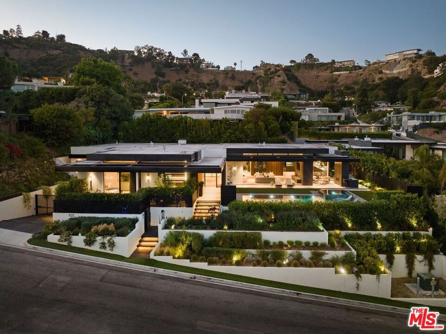 Nestled in the renowned Bird Streets of Doheny Estates, this luxurious mid-century-inspired private residence offers a turnkey experience with curated original art, designer furnishings, and finishes. Spanning at almost 11,000 square feet, it showcases stunning city lights, ocean, and jetliner views from all main entertainment areas. The motorized Fleetwood pocket doors seamlessly blend indoor and outdoor living, while the main foyer features a breathtaking 20-foot glass atrium with a floating staircase wall and oversized Italian mosaic travertine tiles. The open floor plan, bathed in natural light, connects the Miele gourmet kitchen, formal dining room, and spacious living room with a Du Chateau wood slat ceiling and clear-story windows. Outside, the pool pavilion offers a covered patio, fireplace, and porcelain-tiled pool and spa. The primary suite boasts dual baths, closets, and romantic city views, while three ensuite guest rooms provide privacy and garden patios. The lower level features additional guest quarters, a great room, temperature controlled wine display, billiards, an office, a home theater, and a 1000 sq ft wellness spa with a sauna, massage room, steam shower, and dipping /plunge pool. The property also boasts a climate-controlled 8 car garage with car turnstile, glass elevator, putting green, Elan smart home automation with top-notch security and a back-up generator. Experience the epitome of modern luxury living, surrounded by nature's beauty, at this Hollywood Hills masterpiece.