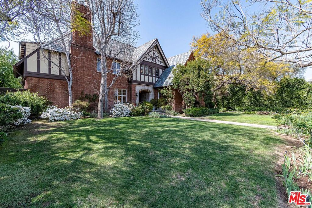Stately Country English Estate for Lease in Hancock Park. Set on one of Hancock Park's finest blocks, this distinguished Country English estate blends timeless architectural beauty with expansive, park-like grounds. A grand entry leads to a sun-filled living room, a formal dining room, a wood-paneled library with hidden bar, and a classic kitchen with separate butler's pantry. A cheerful breakfast room overlooks the gardens, while two bedrooms with a shared bath and a powder room complete the main floor. Upstairs, the spacious primary suite is joined by three additional bedrooms, original bathrooms with exquisite detailing, and a private office. The lower level features a true rarity your very own English pub. Outdoors, the private gardens offer a large sunny pool with spa, sprawling lawns, a built-in BBQ area, and a three-car garage topped by a charming guest apartment.