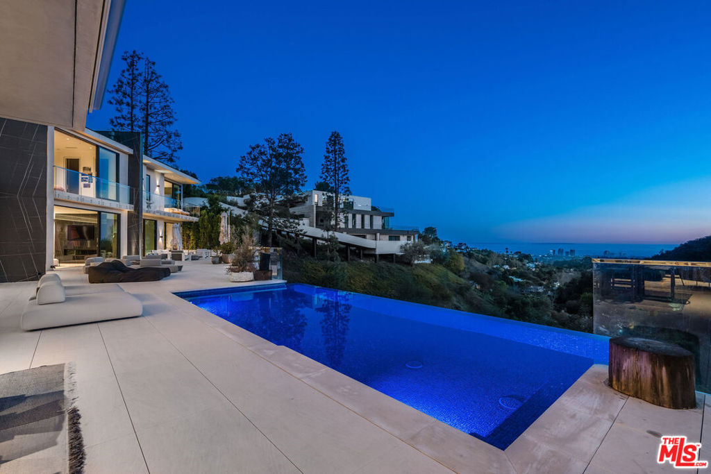 This organic contemporary masterpiece in prime Bel Air is a private retreat with breathtaking views stretching from lush canyons to the city skyline and ocean. Designed with a seamless blend of warm modern aesthetics and natural materials, the home embodies elegance and tranquility. Expansive, light-filled spaces feature floor-to-ceiling Fleetwood doors, creating an effortless indoor-outdoor flow to a 3,000-sqft deck, infinity pool, and a full outdoor kitchen with a pizza oven perfect for luxurious entertainment. The outdoor dining area has heaters and an electric shade for use all year round. The custom kitchen includes reclaimed French Oak cabinetry, Italian stone, Miele appliances and a Wolf gas chef's stove with solid oak pendants by Ross Gardam to enhance its sophisticated yet organic feel. The primary suite is a serene retreat with a private balcony and spa-like custom bath featuring French reclaimed oak cabinetry, custom blackened steel and fluted glass shower doors, and Italian Gessi fixtures all contributing to its natural, understated luxury. The powder room continues this aesthetic with a tone-on-tone design including custom grey stained solid oak walls and a grey concrete vanity. Throughout the home, solid rustic oak accent walls, stained black in the bar, bring warmth and texture complimented by Apparatus lighting in the entry, dining room and primary suite. The home has Crestron/Sonos sound system throughout and Lutron lighting to enhance the ambiance. There are 5 en-suite bedrooms, two additional bathrooms, a home office, theater, gym, wine room, laundry on two levels and off-street parking for 6 cars. A rare opportunity to own an architectural gem where organic beauty and spectacular views meets modern luxury, offering an unparalleled lifestyle in an exclusive community.