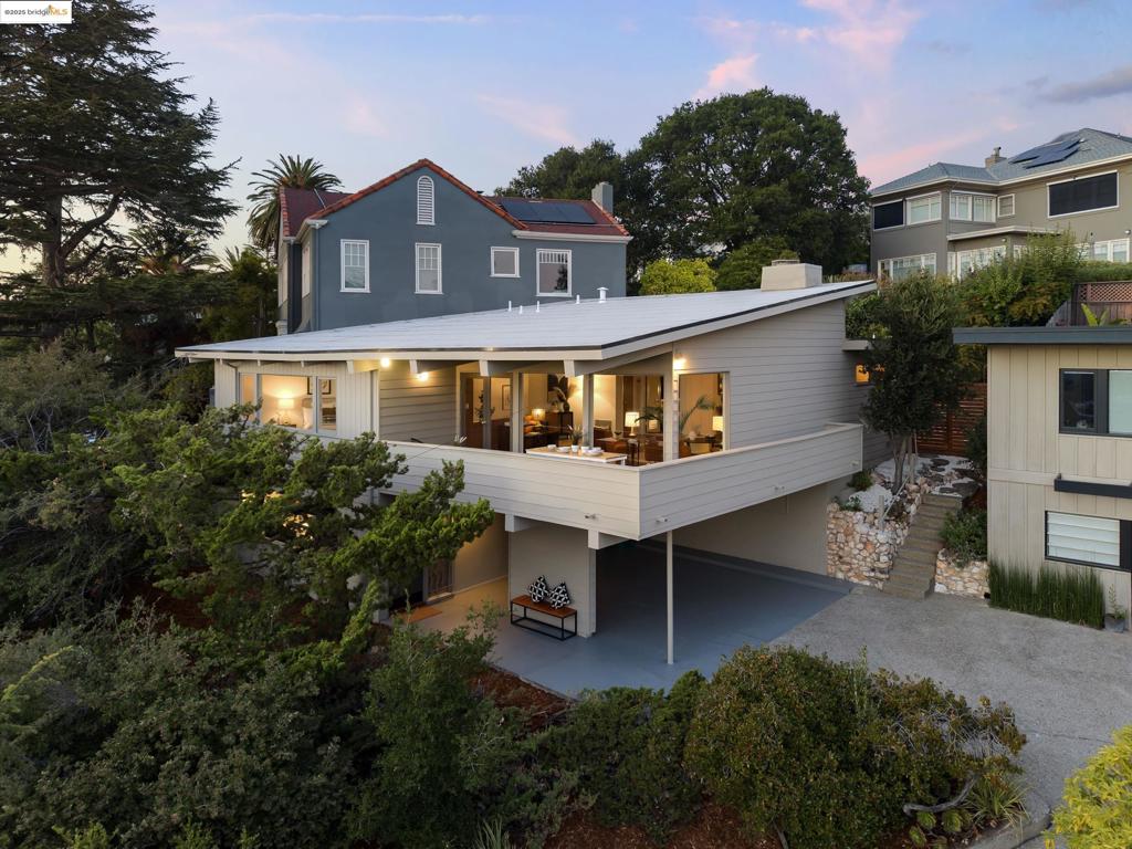 Perfectly placed in the Claremont between Elmwood and Rockridge, this Midcentury gem is a rare example of thoughtful preservation. Just a short walk to Rockridge BART or Star Grocery, the home is perched to take in sweeping views of San Francisco and the Oakland port, best enjoyed from the covered front deck—whether over dinner or as an open-air workspace.Cantilevered with striking Midcentury lines, the three-bedroom, two-and-a-half-bath design balances drama and livability. A soaring, wood-paneled living room with exposed beams and a flagstone fireplace—anchored by a teak mantle and built-in planter—opens to a generous dining area, with double doors extending to the private backyard patio.The kitchen’s vintage yellow tile counters and Dutch door lend warmth and function. Entry-level guest quarters feature a preserved yellow-tiled bath beside a full laundry. Upstairs, the primary suite captures stunning vistas with two large closets, a dressing room, and an original pink-tiled bath—a hallmark of Midcentury design. A third, triangular bedroom with its own half-bath offers flexibility as a retreat or home office.Parking for two cars is tucked below, accessed via a shared private drive.