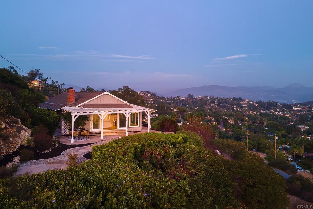 Cozy cottage vibes nestled within the hills of Mt. Helix with spectacular PANORAMIC VIEWS from the mountains to the ocean. Winding stone pathways and rock walls encompass the charm and character of this SINGLE LEVEL 2 bedroom (+ optional room over garage), 2 bath home which offers peace and privacy….Your perfect retreat away from the modern world. Vaulted wood beam ceilings and floor to ceiling windows highlight the open concept floorpan allowing you to appreciate views from every room. Seamless indoor/outdoor living lets you enjoy the sunrise on the front porch or sunset dinners on the patio. Spacious kitchen boasts stainless steel appliances and a breakfast nook while the formal dining is open to the living room showcasing hardwood flooring and decorative fireplace. Additional features include multiple split systems throughout, custom window coverings and a large California room that includes the laundry area and extra space for storage if needed. Bonus room above the garage makes for a great home office, man cave/she-shed, playroom, etc. Oversized 1-car detached garage plus 2 carports provide ample parking and is conveniently located at the end of a cul-de-sac. Property is on sewer and fully electric!