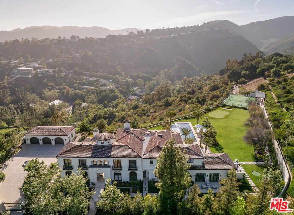 The Westside's most exclusive offering - a rare and exciting opportunity to acquire an extraordinary tennis estate in the ultra-private enclave of Brentwood Country Estates, the guard-gated community of just 13 homes known for its unmatched 24/7 security, privacy and gorgeous views. Gracefully sited on its own five acre promontory, behind its own gates, this truly one of a kind property, completely reimagined and redesigned, is offered fully furnished, ready to welcome you in time for summer. When you arrive, you are overtaken by a sense of serenity, peace and calm. Taking your first breath of the mountain air, you can feel yourself starting to relax. Where else west of the 405, can you live in your own five star resort and enjoy the low key comforts of home? A "welcome home" lounge area is the first "Oh wow" moment, leading through the property to the many curated outdoor areas, each providing private spaces for different ways to enjoy the ultimate California lifestyle. The gorgeous pool and spa invite you to luxuriate in the afternoon sunshine. Surrounding the pool, the expansive lawn offers a fun putting and chipping green. Beyond through the olive tree lined walkway is a sunken and lit tennis court, easily converted for pickleball and basketball, with a viewing pavilion complete with its own changing room and bath. The property is beautiful during the day, but in the evening it absolutely glows with gorgeous lighting and music everywhere. The approximately 9960 square foot interior is filled with natural light and stylish sophistication. The sightline of the entry hall previews great things to come, and it does not disappoint. The entry leads to the formal living room and expansive dining room, flanked by a beautiful office all with floor to ceiling windows offering views of the perfectly manicured grounds. The heart of the home is the chef's kitchen with a spacious breakfast area with its own big screen TV, temperature controlled wine room, and oversized island, with all the best high end appliances, double Wolf range, double side by side Dacor refrigerators, three sinks, and "they thought of everything" butler's pantry. Right outside the kitchen facing the mountains, through two sets of French doors, the barbecue and outdoor dining areas provide the perfect venue to gather under the stars and watch the moonrise. Adjacent to the kitchen is a fabulous family room, designed for pool, backgammon or just hanging out until dinner is ready. Motorized black-out drapes can convert this space for snuggling up on a comfy sectional to watch your favorite movie. The first level also features a large guest suite, and commodious laundry room with double appliances, a mud room and plenty of storage. On the second level, the dreamy primary suite offers a sanctuary with peaceful views to the sky and mountains, reminiscent of your last great trip to Tuscany or Provence. Tons of mirrored closets and built-ins separate the two sides to the bath area, connected by a distinctive wet room double shower and tub. Three additional ensuite bedrooms provide comfort and privacy for guests or family, and a fully equipped gym completes the upper level. The entire home is powered by a state-of-the-art Crestron smart system, offering seamless control of lighting, music, climate and security with cameras everywhere. In addition to the oversized three car garage, the circular motorcourt is large enough to accommodate ten cars. Located in lower Mandeville Canyon, Brentwood Country Estates, provides easy access to Santa Monica, and other areas of the Westside, with wonderful restaurants, shops, hiking trails, golf and the beach minutes away.