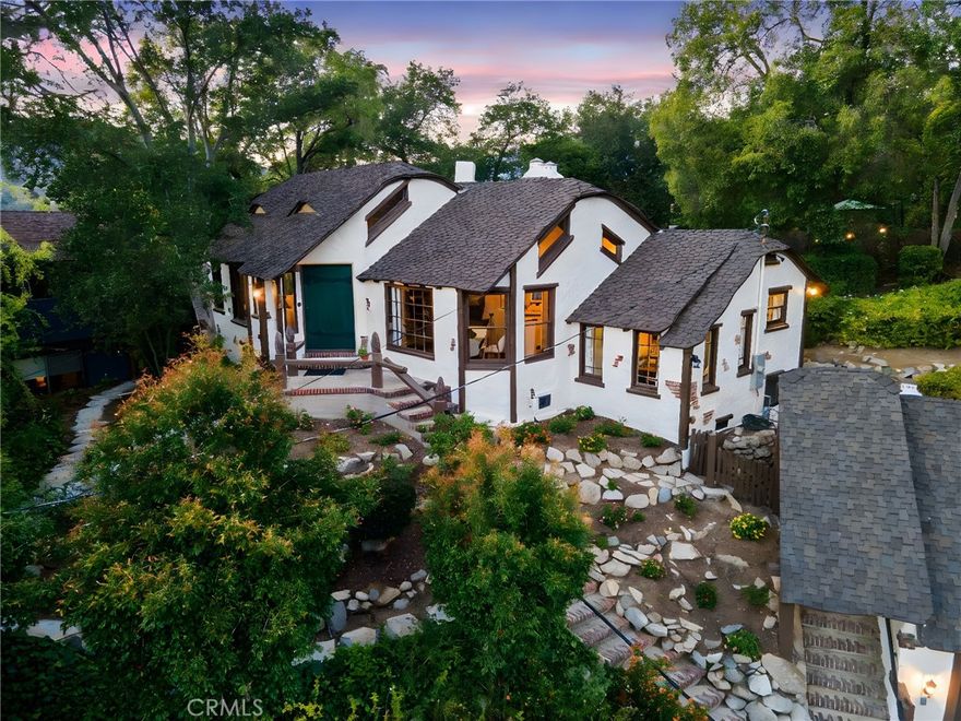 The MacBride House (1924) — A rare 3-bedroom, 2-bathroom, 1,552-square-foot Storybook Tudor tucked into the trees of Glendale’s Verdugo Woodlands, revived through a meticulous two-year restoration that brought back its original soul while introducing modern comfort. Soon to be officially recognized under the Mills Act, this home offers not only a connection to Glendale’s architectural heritage but also the rare potential for significant long-term property-tax savings for its next owner. Built by an English craftsman who once worked for early Hollywood film studios, this home feels like it was lifted straight from Disney’s Snow White, with whimsical rooflines, arched doorways, and hand-carved details that radiate storybook magic. Inside, vaulted open-beam ceilings and leaded-glass windows fill the grand living hall with soft light that glows across refinished wood floors. The clinker-brick inglenook fireplace, flanked by original hand-carved benches, stands as the heart of the home and a masterpiece of 1920s design. The kitchen and baths have been restored with an artist’s restraint, new time period inspired wallpaper, reglazed sinks, new distressed vintage flooring in bathrooms and kitchen and new classic fixtures chosen in a way to preserve the home’s authenticity. Behind the beauty, every system has been thoughtfully modernized, including new copper plumbing, updated electrical, dual-zone HVAC, and an EV-ready two-car garage with a finished attic loft perfect for a creative studio or private retreat. The 10,226-square-foot lot unfolds into a private paradise of meandering garden paths, intimate patios, and mountain views that make you feel completely tucked away from the world while still only five minutes from the conveniences of modern life. Even the back staircase carries a homage of Glendale’s story, built from old railroad ties that reflect what once supported the trolley network that brought residents to this hillside haven a century ago. The Glendale Historical Commission has already met and formally recommended the home for Mills Act approval, with final City Council confirmation expected soon, offering the next owner both the pride of preservation and the potential for long-term property tax savings. The MacBride House is more than a home; it is a living story; a fairytale refuge that celebrates craftsmanship, imagination, and the timeless beauty that first made Glendale one of California’s most enchanting communities.