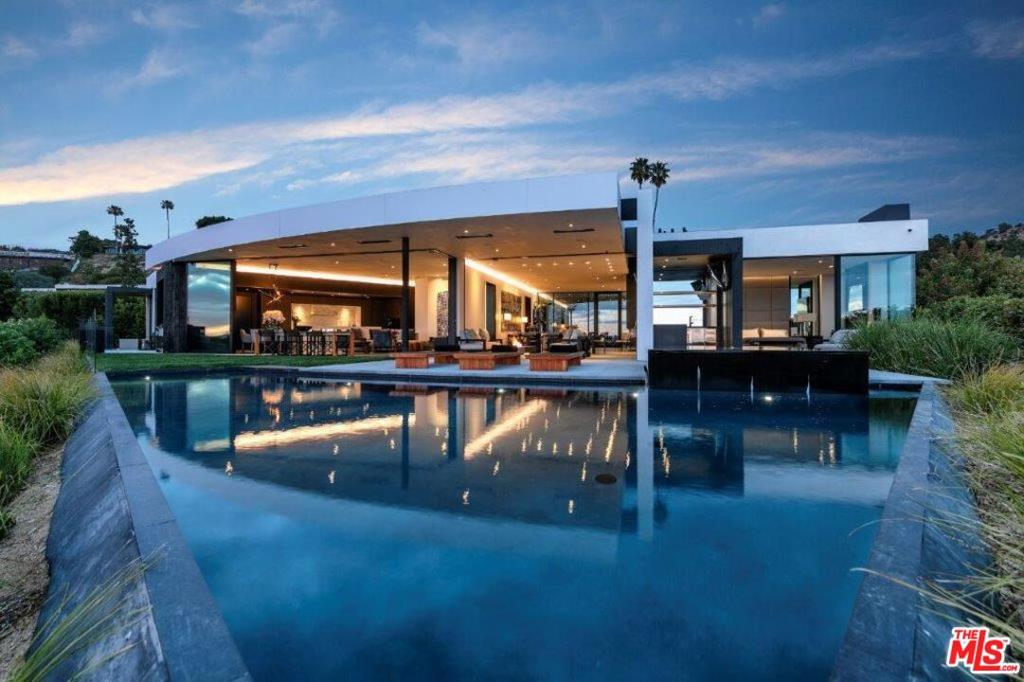 A spectacular hillside glass-walled sanctuary by design icon Mark Rios with Trousdale Estates most explosive panoramic city to ocean views. Interiors by Dusenbury Design, this modern organic masterpiece provides the most captivating entertainment features. Behind the privacy of a 13-ft architectural wall, the 12,456-sf, 6-beds, 11-baths estate boasts a 15-ft waterfall in the front court cascading into a lower-level reflecting pool & a 2100-sf subterranean garage. Elegant, clean lines reflecting mid-century modern sophistication meet luxurious stone, wood & marble finishes. Floor-to-ceiling doors & elegant open concept fill every inch of the main living spaces with natural light and unobstructed views. Chefs kitchen, breakfast bar, formal & alfresco dining. Outdoor entertainment features a firepit lounge with a bar and a lush terrace with an expansive pool/spa soaring over the skyline. Lower-level entertainment oasis features a stunning blue velvet lounge with a marble bar, an oversized glass wine cellar & a theater with matching palette. Lavish 1,600-sqft primary suite features dual bathrooms with a tranquil tub overlooking the 360 vista. Additional amenities include gym, massage, elevator, beauty salon, en-suite guest rooms & staff quarters. Make your mark among the most discerning elite with this legendary home.