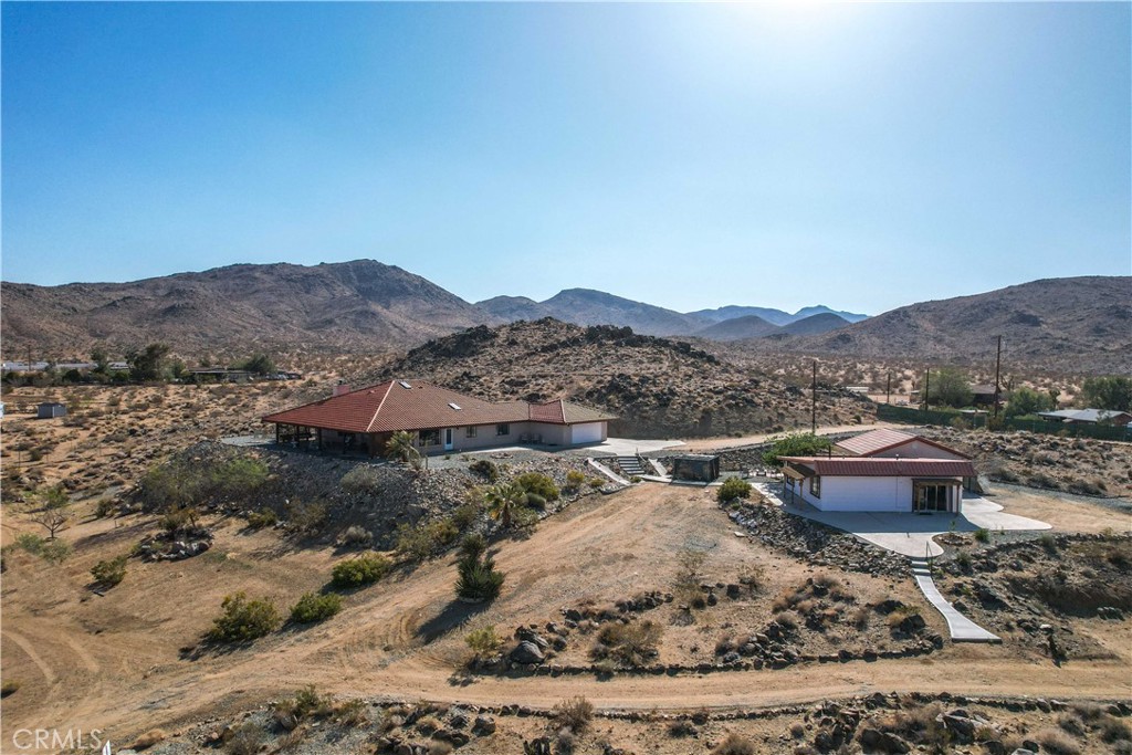 You will be amazed at the stunning views when you arrive. This one-of-a-kind property has two homes nestled against natural rocks. Main home has 2 bedrooms, 2 bathrooms, and a large great room with wood-beamed vaulted ceiling. Extraordinary views from windows on 3 sides. Kitchen has Corian counters with tons of cabinets. L-shape kitchen island has bar seating. Two large bedrooms with 3 walk-in closets. Huge soaking tub in the master bath. There is a south-facing sunroom which is perfect for soaking up the winter sun. The indoor laundry room has plenty of cabinets for all your storage needs. 2 car attached garage. The front patio runs the length of the home and provides endless eastern views. This home is perfect for hosting large parties or gatherings. The 2nd home has 1 bedroom, 1 bath with an enclosed porch. It also has it's own detached 2 car garage. The views from this 2nd home are incredible as well. The entire property of 5 acres is fully fenced with two gated entrances. Property is dotted with Joshua Trees, Palm Trees, Palo Verde trees, and Mojave Yuccas. Natural desert wildlife can often be seen, such as Quail, Rabbits, Coyotes and more. Landers is home to the Integraton, La Copine restaurant and world-famous Gublers Orchids. Popular riding trails nearby. Joshua Tree National Park is a mere 25 minutes away. Big Bear is 1 hour drive. This amazing property is perfect for vacation rental, wedding venue or other creative ideas. Live in one and rent the other. Many possibilities. Make your appointment to view today. Buyer to verify details and zoning etc.