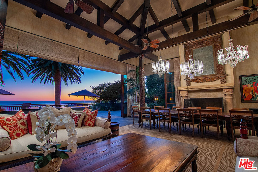 With breathtaking views, Bali-inspired design, and every contemporary comfort, this magnificent estate is a serene sanctuary for exquisite living and impressive entertaining. The private, gated property of over 1.2 acres extends from PCH to Malibu Road, perfectly landscaped and commanding expansive ocean views. A long palm-lined drive leads past a two-story, two-bedroom guesthouse, a lighted north-south tennis court and pavilion, and a fountain, waterfall, and gardens before arriving at the enormous motor court and four-car garage. A dramatic gateway and long, serene palm-lined reflecting pool lead between the wings of the U-shaped house to the gorgeous double-door entry. With interiors designed by Martyn Lawrence Bullard and stunning sight-lines to the ocean, the house is detailed with ornate wood carving, very tall beamed ceilings, wood and stone floors, and full-width exterior doors that vanish to offer seamless flow between indoors and out. The entry steps down to the formal living room, which includes a generous dining area, a pair of facing fireplaces, and a wall of glass that opens onto a roomy patio with a fireplace, stunning ocean view, and a nearby fountain and barbecue island. Adjoining the living room is a spectacular ocean-view great room that includes a family room with fireplace, dining area, and a gourmet kitchen with a huge stone-topped island with seating, deeply recessed tray ceilings, beautiful cabinetry, and a pantry. One wing of the house has two bedrooms and a laundry room. The other wing features a majestic ocean-view owner's retreat with high wood beamed ceilings, beautiful wall coverings, wood floors, and a wide glass doorway opening to a tranquil covered patio. A hallway leads to a luxurious bath, two very large closets/dressing areas, and, at the end of the hall, a resplendent Bali-inspired library/study with high coved ceilings, a wall of built-in book shelves and cabinets, a fireplace, and doors to the patio and to a private sitting area. The home's lower level features a party-perfect bar room highlighted with ornate metalwork that encloses a large wine storage area. The bar extends into a spacious tiered home projection theater. A long hallway leads to a second powder room, a changing room, and another bar, which opens to the lower patio, spa, sitting areas, and lawns, as well as the infinity ozone pool, patio, cabana, and private steps to Malibu Road and access to the beach/ocean. With Crestron electronics and full-house water filtration, this remarkable estate is a livable legacy.