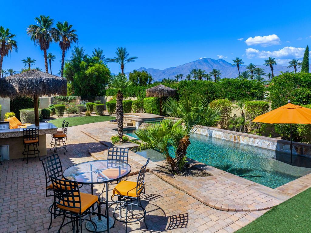An exceptional opportunity to own a private resort-style estate in the heart of La Quinta's exclusive Palms Golf Club. Nestled behind the gates of this boutique, low-density golf community, this sprawling compound spans over half an acre and is thoughtfully designed for luxurious desert living, effortless entertaining, and ultimate privacy.Surrounded by mountain vistas and lush, manicured grounds, the main residence offers approximately 5,000 square feet of open-concept living space, featuring 6 bedrooms and 5 bathrooms, including two expansive primary suites with spa-like en-suite baths and generous walk-in closets. The light-filled great room--with its dramatic ceilings, inviting fireplace, and seamless indoor-outdoor flow--connects to a chef's kitchen outfitted with slab granite countertops, stainless steel appliances, and an oversized island perfect for casual meals and lively gatherings.Guests are treated to their own private havens with three attached casitas--each offering either a kitchenette or a separate living room, en-suite or shared bathroom, and dedicated entrances from the central courtyard, allowing for comfort, flexibility, and total seclusion.The outdoor spaces are equally impressive. Enjoy resort-caliber amenities including a sparkling pool and elevated spa, misting system, putting green, lighted palapas for evening lounging, a firepit, and a fully-equipped outdoor kitchen with bar seating. Whether hosting a crowd or enjoying quiet evenings under the stars, the home is tailored for year-round enjoyment.Additional highlights include two separate two-car garages, a dedicated golf cart garage, and ample guest parking--combining function with thoughtful design.Located within The Palms Golf Club, where membership is optional, residents may access one of the desert's most revered private courses--co-designed by Masters Champion Fred Couples and renowned architect Brian Curley. The intimate clubhouse features three dining venues, a welcoming bar, a fully stocked golf shop, and a vibrant social calendar, making it a hub for both recreation and community.All just minutes from world-class golf, dining, shopping, and hiking, with quick access to Interstate 10 and the greater Coachella Valley. This one-of-a-kind property is the perfect desert escape--offering space, sophistication, and the rare combination of privacy and connection.