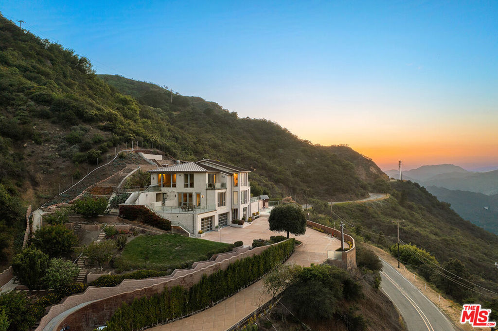 Welcome to 25155 Piuma Road - a one-of-a-kind architectural masterpiece by acclaimed architect Jack Moses, perched on a private promontory in the Malibu hills. Set behind gates and surrounded by a mile of open space with no neighboring homes in sight, this striking modern retreat offers unmatched privacy, tranquility, and panoramic views of the Santa Monica Mountains and Pacific Ocean. Often described as a "sanctuary in the sky" or "a house in the clouds," this home is truly unlike any other and simply cannot be duplicated. Expansive walls of glass flood the interiors with natural light and frame breathtaking vistas from nearly every room. The open-concept living area features wide-plank hardwood floors, a sleek fireplace, and seamless indoor-outdoor flow to multiple terraces. The chef's kitchen is outfitted with top-of-the-line appliances, custom cabinetry, and a large island ideal for entertaining. This multi-level estate offers generously sized bedrooms, including a luxurious primary suite with spa-like amenities, a soaking tub, and jaw-dropping views. Additional features include a media room, home office, and ample guest accommodations. The outdoor spaces are nothing short of spectacular, with a resort-style infinity pool and spa, expansive decks for lounging and dining, a pergola-covered firepit lounge, and beautifully curated gardens featuring 26 fruit and citrus trees. Environmentally conscious buyers will appreciate that the home is set up to be completely off the grid, with a reverse osmosis water filtration system and a private well that pumps water from 200 feet below into two 5,000-gallon storage tanks, providing clean, free water year-round. Tucked within the Santa Monica Mountains National Recreation Area, yet just 10 minutes from both Calabasas and Nobu Malibu, 25155 Piuma Road offers the perfect blend of secluded luxury and accessible convenience. A rare opportunity to own an extraordinary retreat in the sky, where nature, design, and serenity converge.
