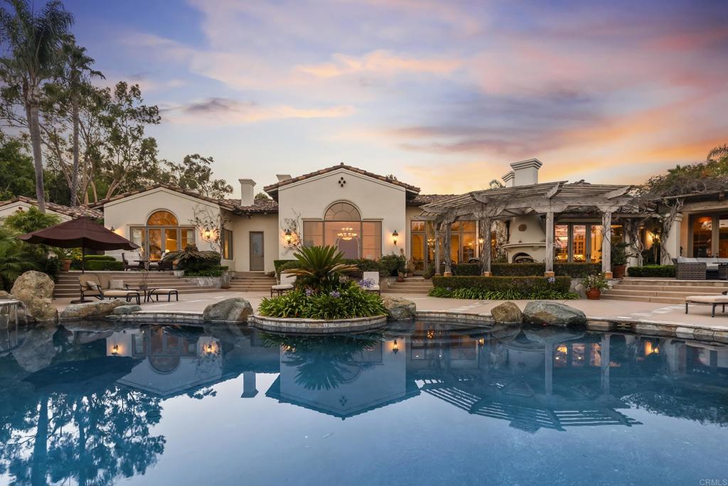 Welcome to 7057 Rancho Cielo, a stunning single-level estate perfectly positioned in the prestigious Covenant of Rancho Santa Fe. Encompassing over three serene acres, this architectural treasure captures uninterrupted southern mountain views and offers a lifestyle defined by privacy, elegance, and effortless California living. Behind a private gated entry, a long circular driveway winds through manicured gardens, setting the stage for the refined residence within. Spanning 8,424 square feet, the home offers both formal and informal living and dining spaces, designed for seamless entertaining and everyday comfort. Walls of glass invite natural light and frame pastoral vistas, while a 160-bottle climate-controlled wine room with adjacent bar elevates gatherings with friends and family. Five bedrooms and seven baths, plus a detached 432-square-foot casita currently outfitted as a gym, provide versatile accommodations for guests, work, or recreation. Outdoors, the resort-style grounds inspire connection and relaxation with a vanishing-edge pool and spa, covered outdoor kitchen, multiple lounge and dining areas, and a charming family orchard. All of this is set within minutes of the Rancho Santa Fe Village, award-winning schools, and world-class golf, making 7057 Rancho Cielo not just a home, but a statement in luxury and the art of single-level living.
