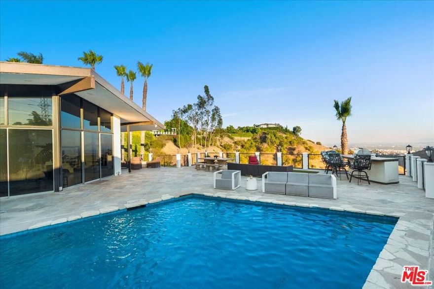 Nestled in the serene enclave of Lakeridge Estates, this immaculate and spacious residence offers the perfect blend of modern luxury and timeless California charm. Situated in the prestigious Hollywood Hills, this 3-bedroom, 2-bathroom home offered both furnished or unfurnished boasts a thoughtfully designed open floor plan ideal for both relaxed living and elegant entertaining. Step inside to be greeted by striking floor-to-ceiling windows that bathe the interior in natural light and showcase sweeping views of the canyon, city lights, and a sparkling pool. A dramatic double-sided fireplace anchors the expansive living and dining areas, seamlessly connecting to a gourmet kitchen outfitted with top-of-the-line Viking appliances, a generous center island, wine refrigerator, wet bar, and additional seating area.The tranquil primary suite features soaring ceilings, a spacious ensuite bathroom, and private sliding glass doors that open to a serene side deck. A second bedroom shares the fireplace and enjoys its own access to the outdoors, while the third bedroom includes an adjoining mirrored bonus space ideal as a home gym, studio, or office. Outdoors, a custom waterfall feature frames the inviting pool, surrounded by ample lounge seating, a built-in BBQ, outdoor shower, and cozy fire pit all set against a backdrop of breathtaking canyon and city views.